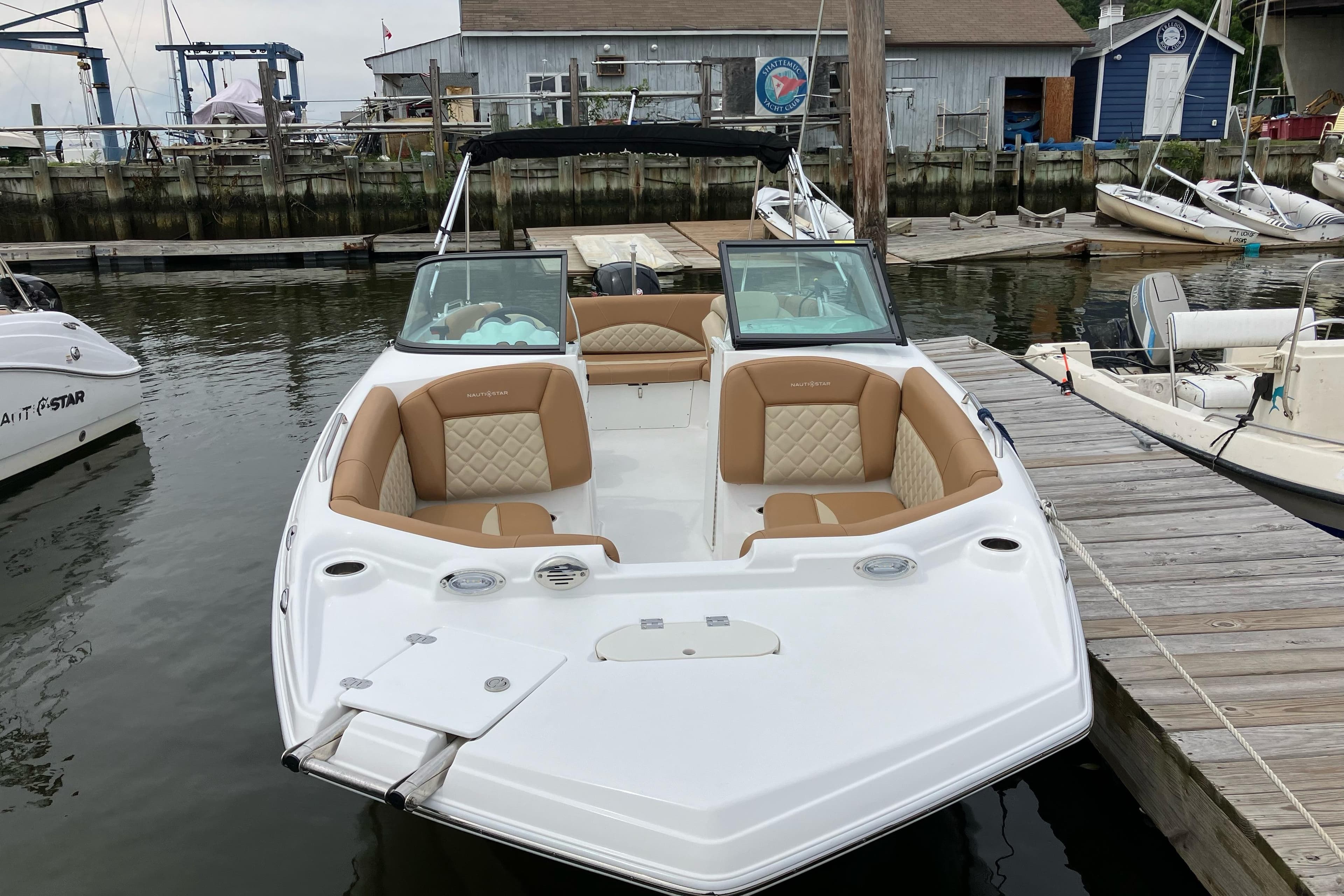 2025 NauticStar 223 DC Deck boat docked at marina, featuring tan seating and sleek design.