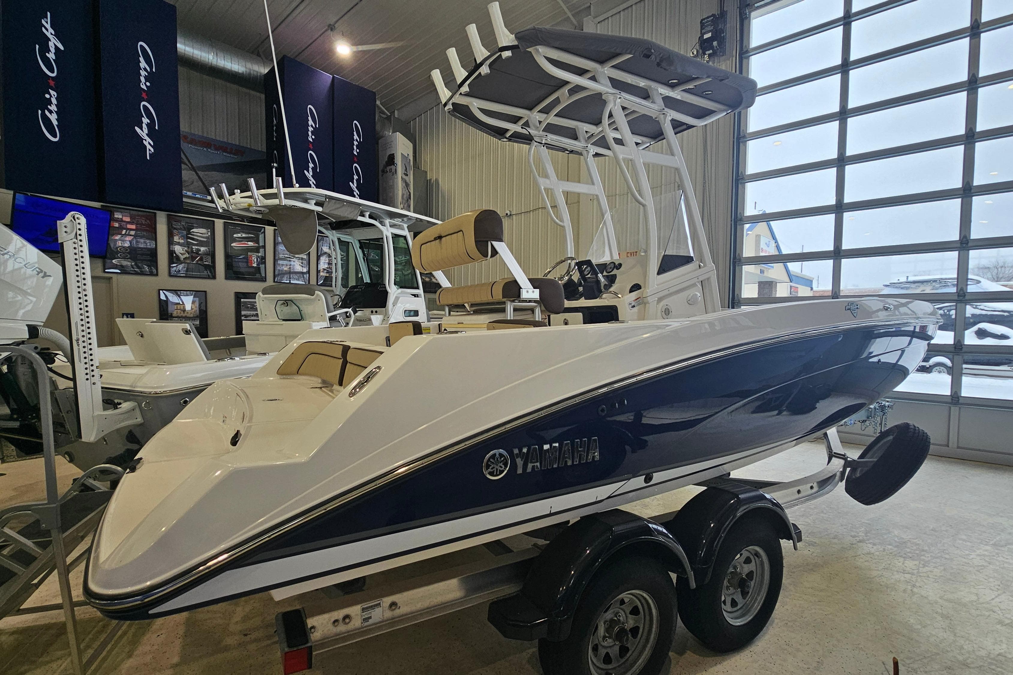 2021 Yamaha Boats 210 FSH Sport in showroom, sleek design, dual-axle trailer.