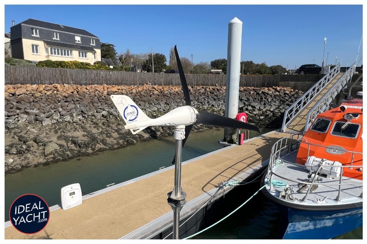 Wind turbine on dock near Lagoon 500 yacht, 2011 model, with lifeboat and coastal backdrop.