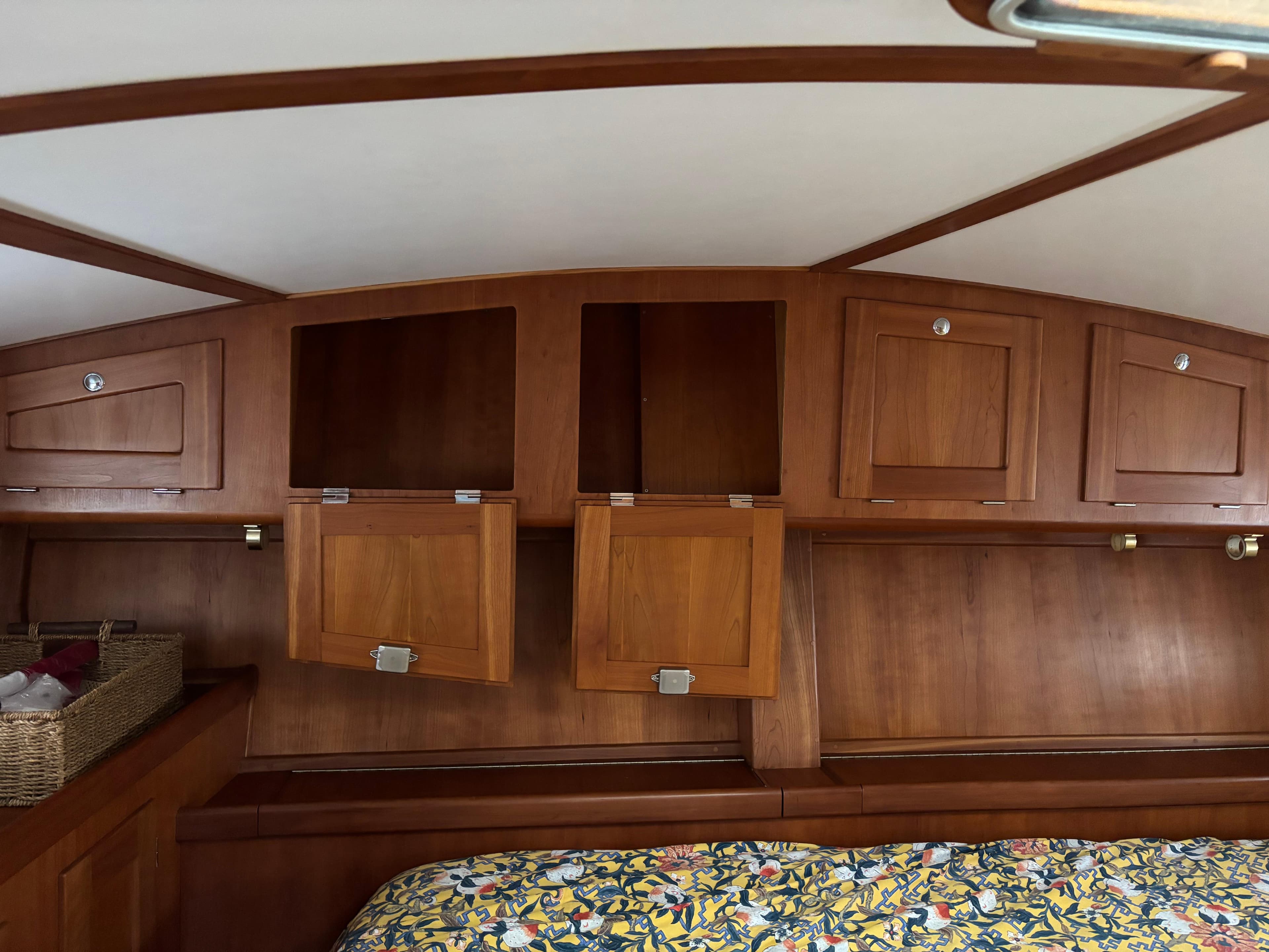 Wooden interior of 1999 Diesel Duck Trawler with storage cabinets and floral bedding.