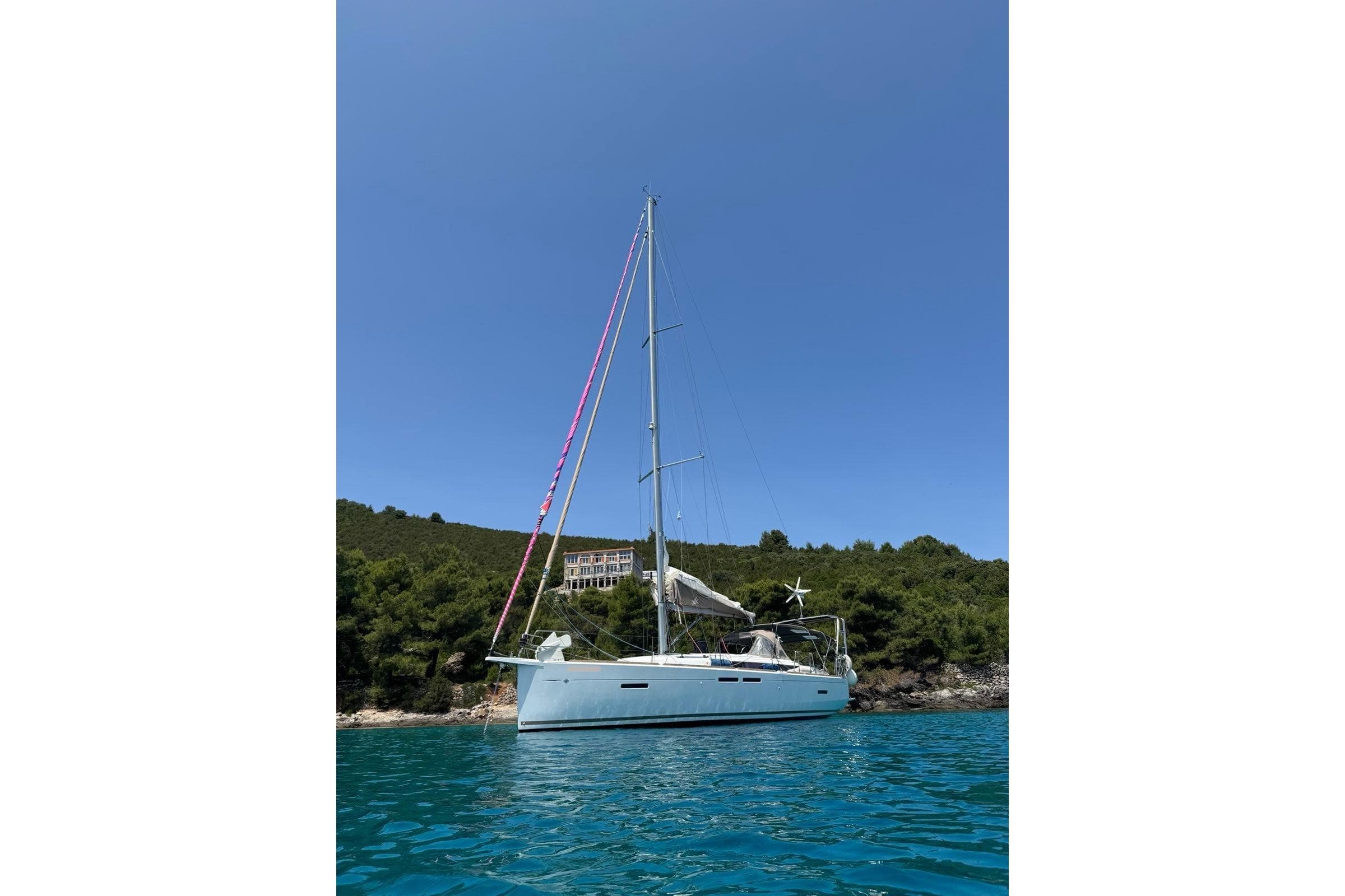 2016 Jeanneau Sun Odyssey 419 sailboat anchored in clear blue water near a lush coastline.