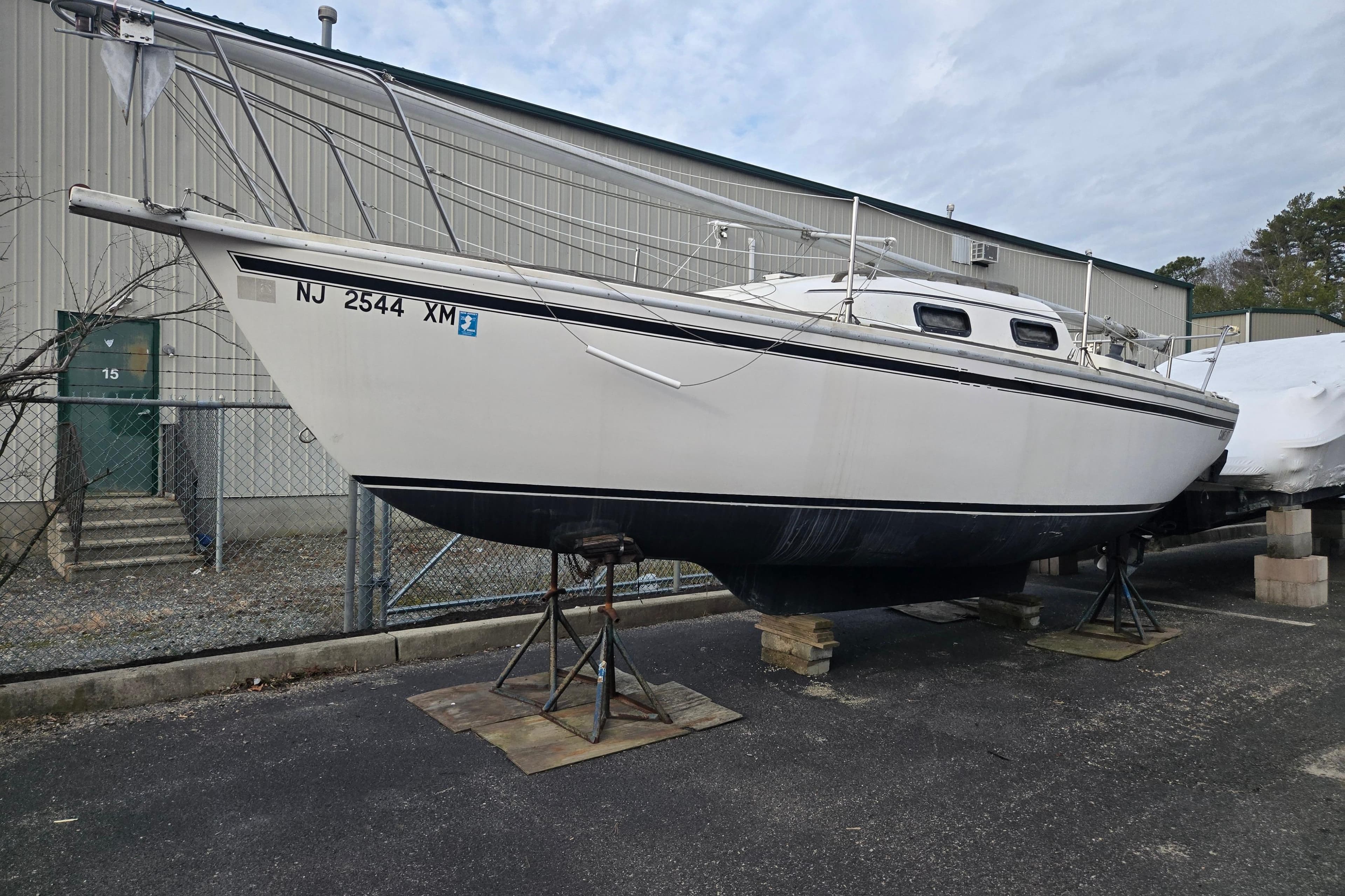 1986 Sovereign 24 sailboat on stands, parked outdoors near a metal building.