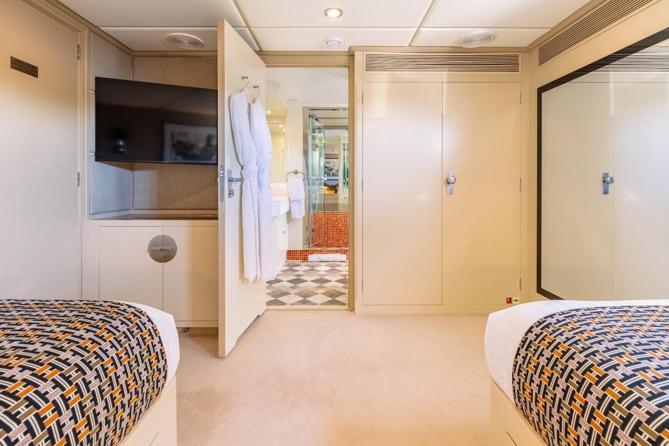 Luxurious 1983 Feadship 55 yacht cabin with twin beds, TV, and ensuite bathroom.
