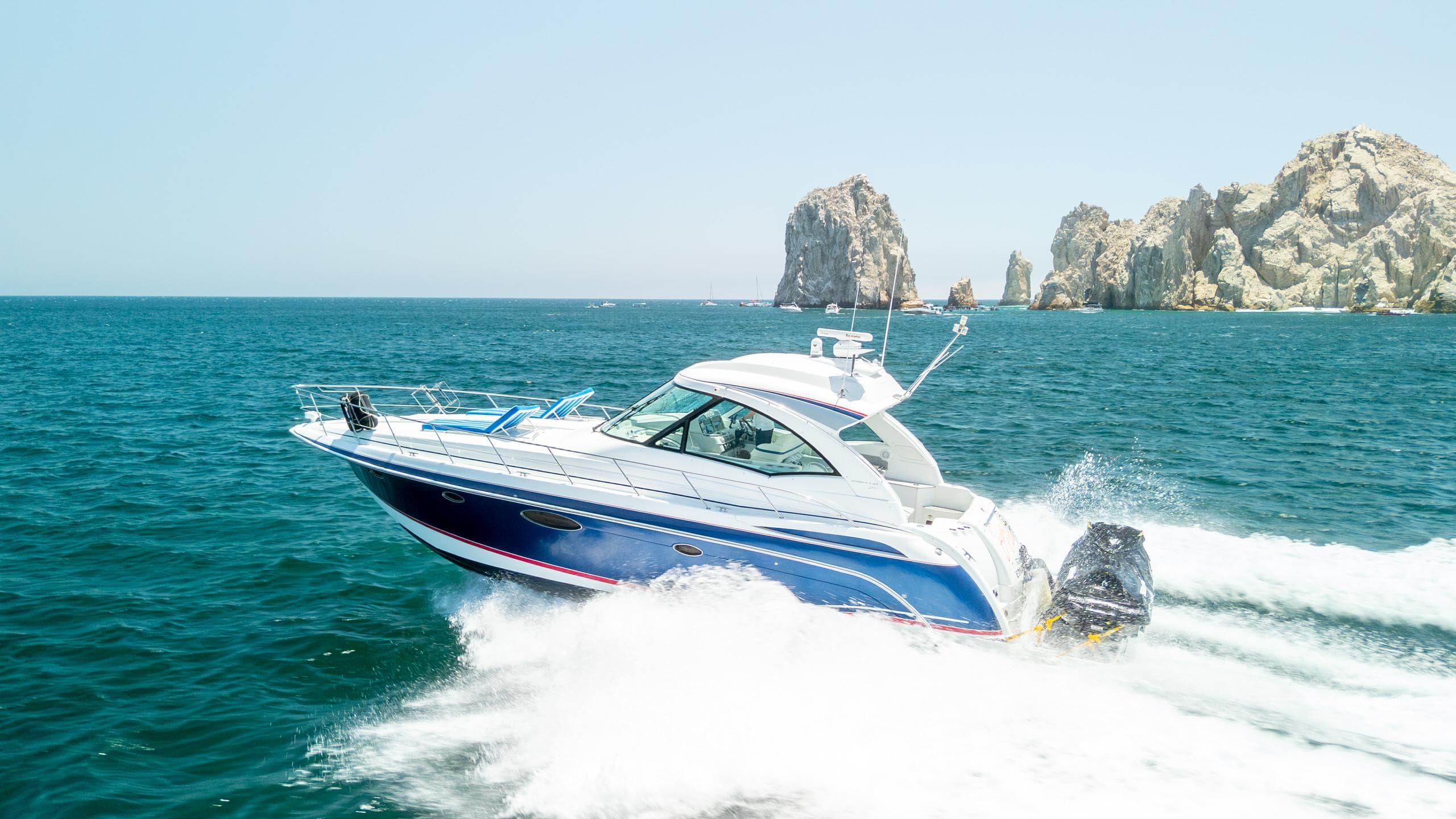 2007 Formula 45 Yacht cruising on blue ocean near rocky cliffs.