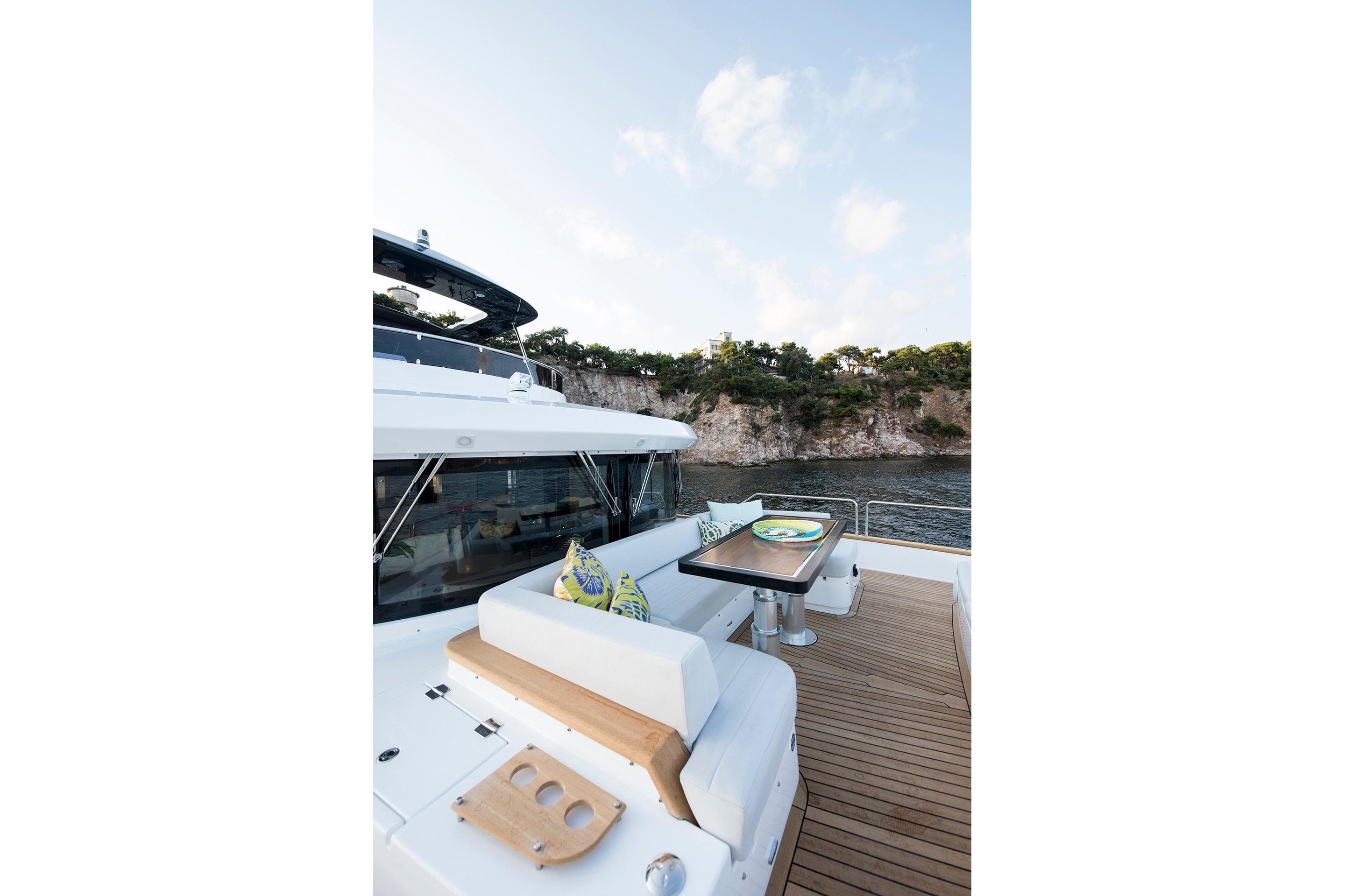 Luxurious Sirena 68 yacht deck with seating, table, and scenic coastal view, 2027 model.