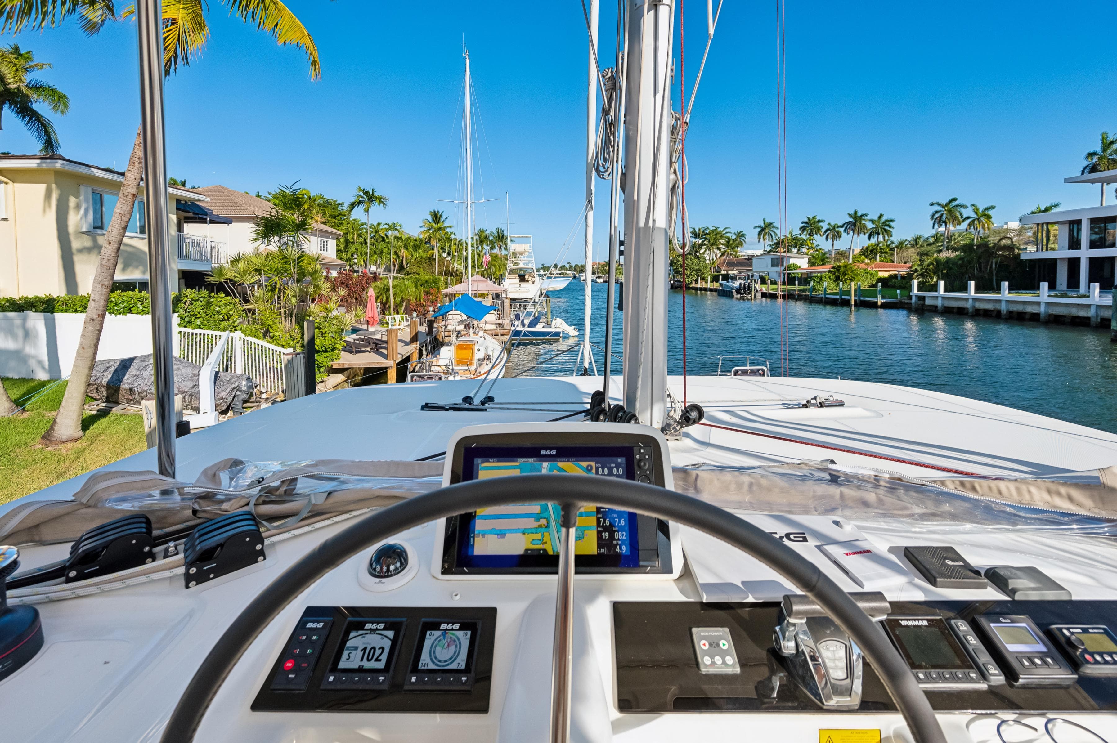 Lagoon 46 catamaran cockpit view, 2022 model, navigating a scenic canal with palm trees.