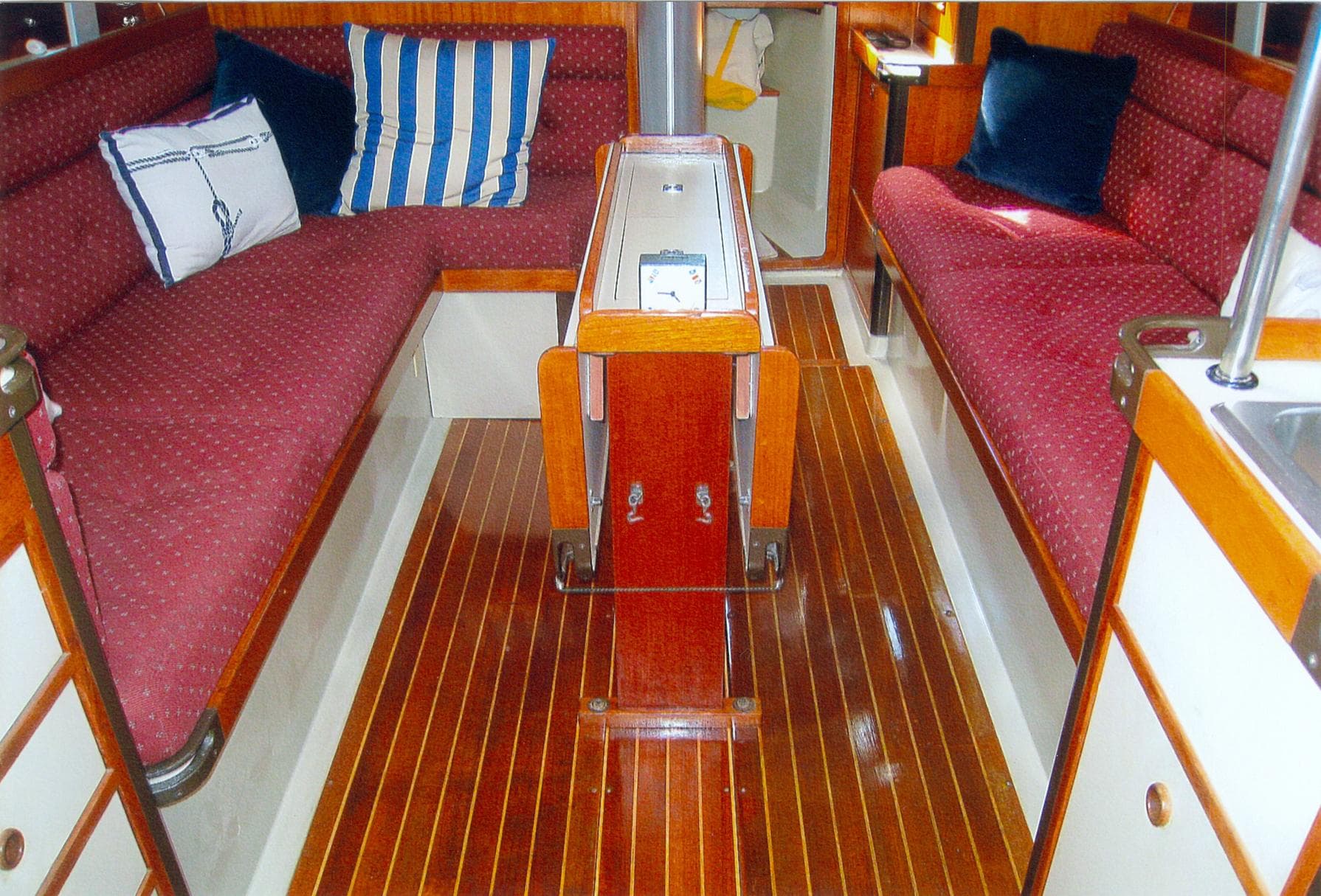 Interior of 1983 C&C 37 sailboat with polished wood flooring and red cushioned seating.