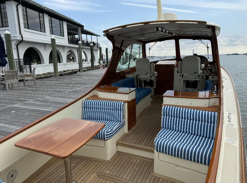 2018 Hinckley Picnic Boat 37 MKIII with striped seating, docked by a waterfront building.