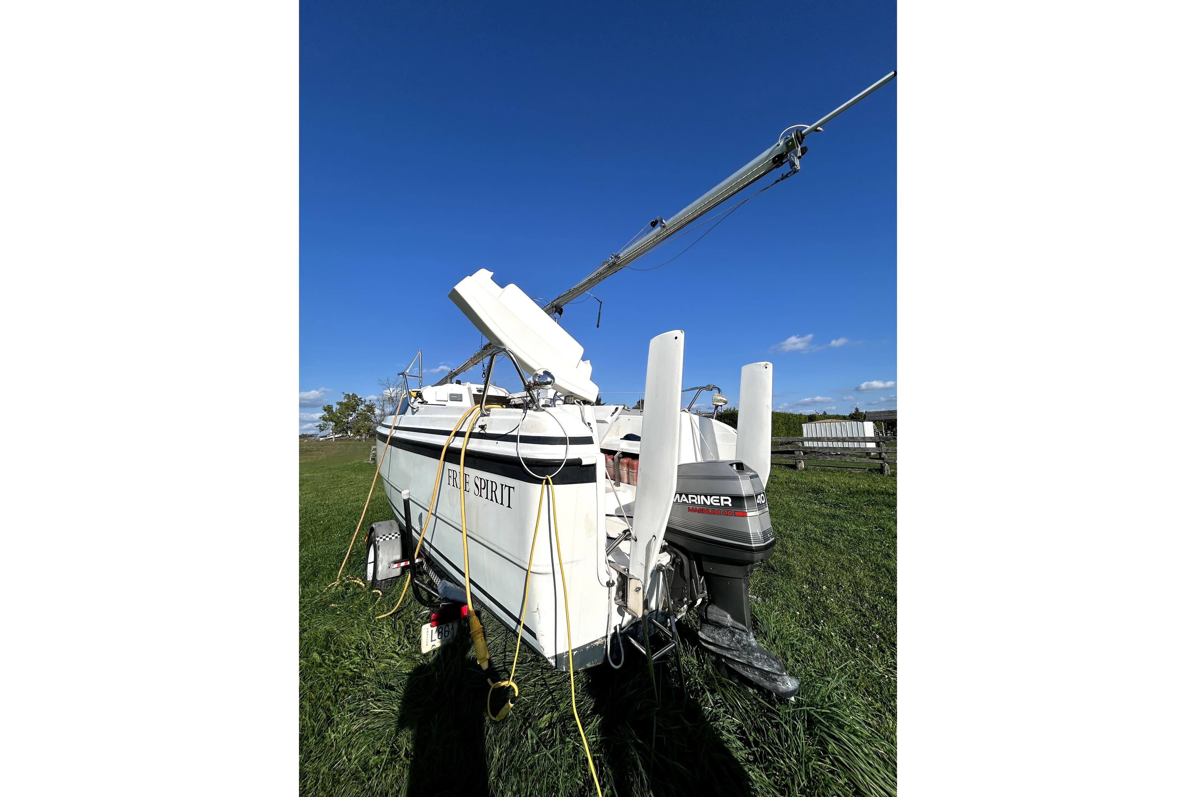 1998 MacGregor 26X Powersailer with Mariner outboard motor on grassy field.