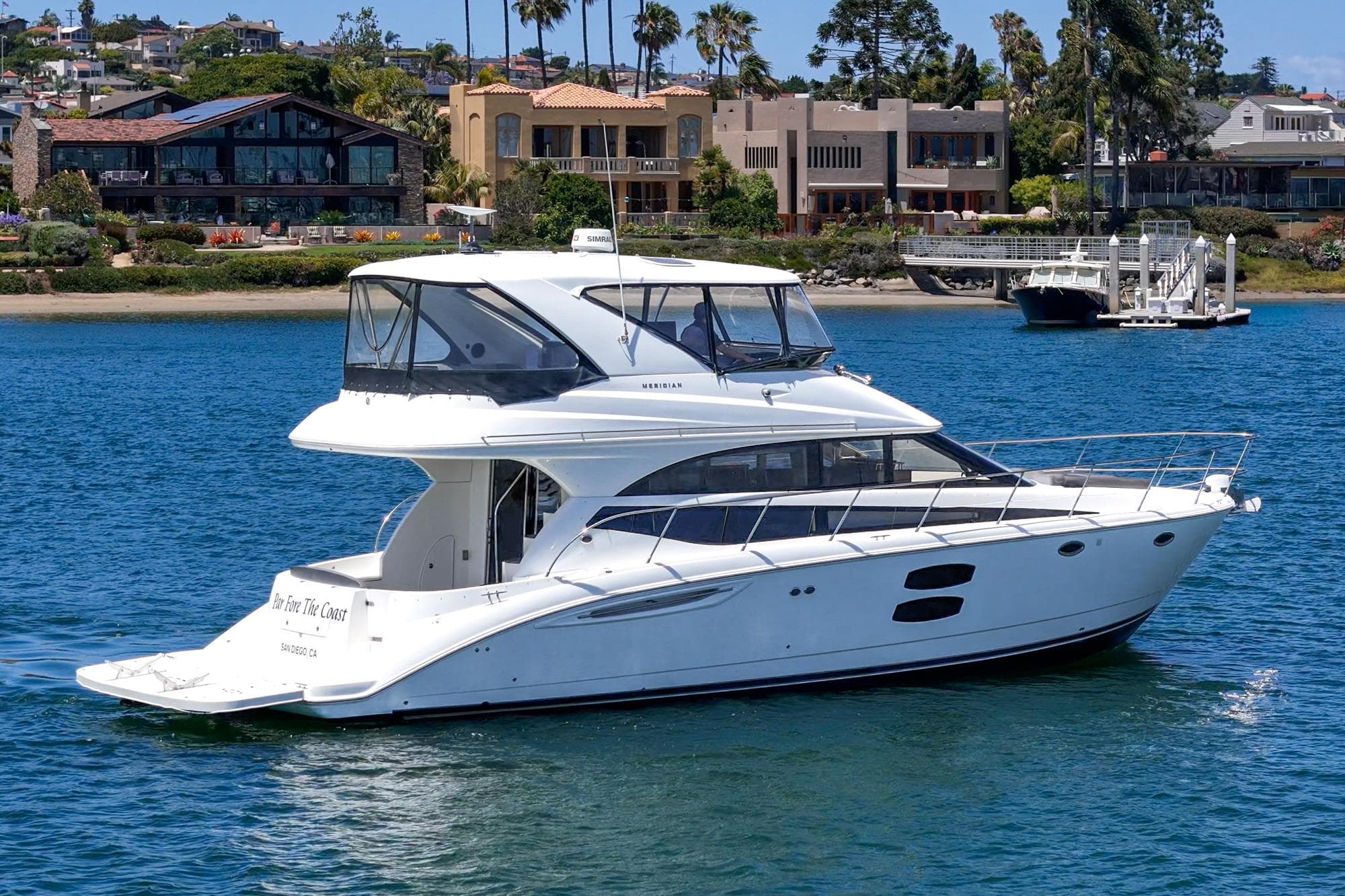 2009 Meridian 441 Sedan yacht cruising on a scenic waterfront with luxury homes.
