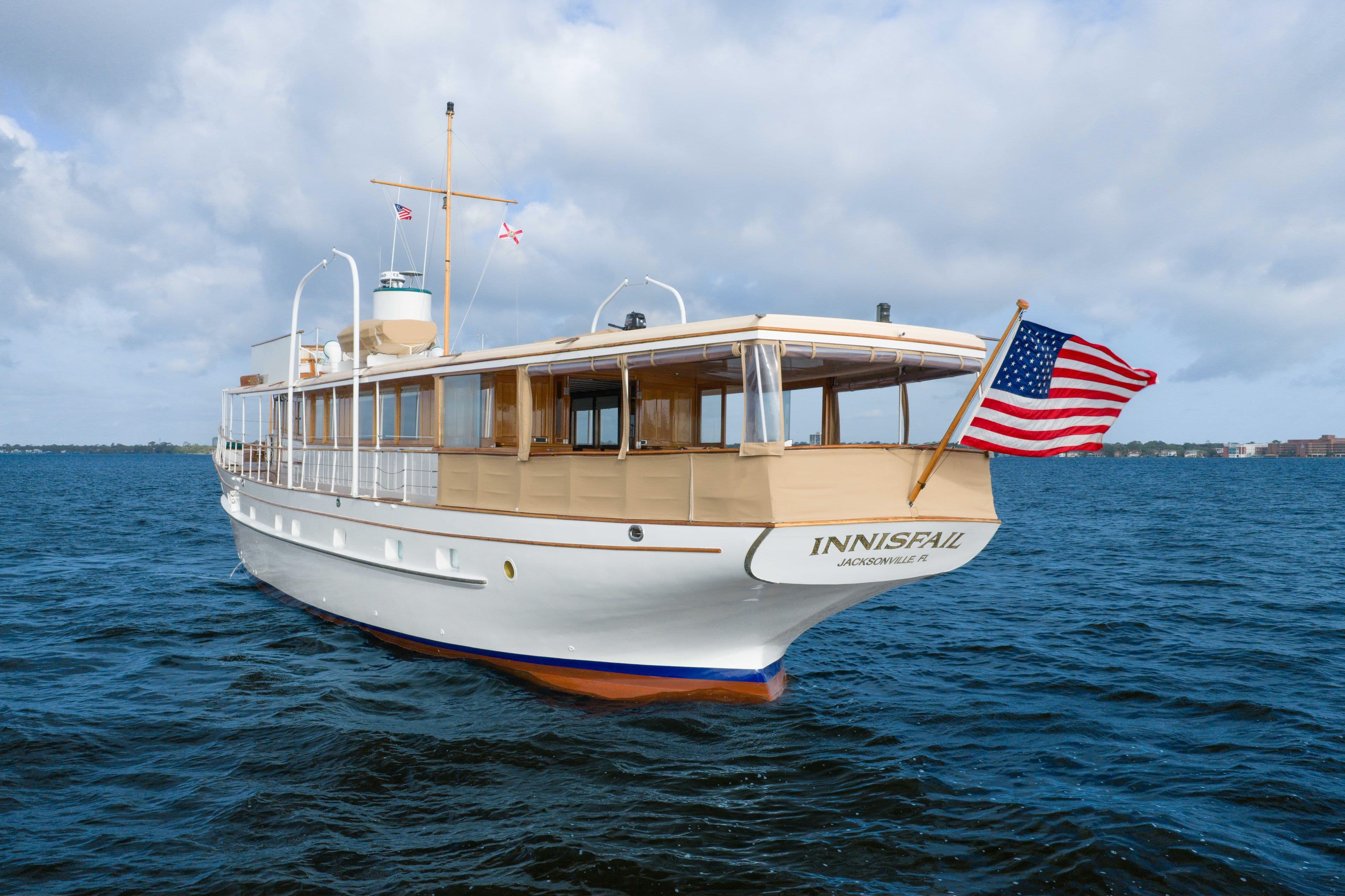 1939 Mathis Trumpy Fantail Houseboat on water, American flag, cloudy sky.