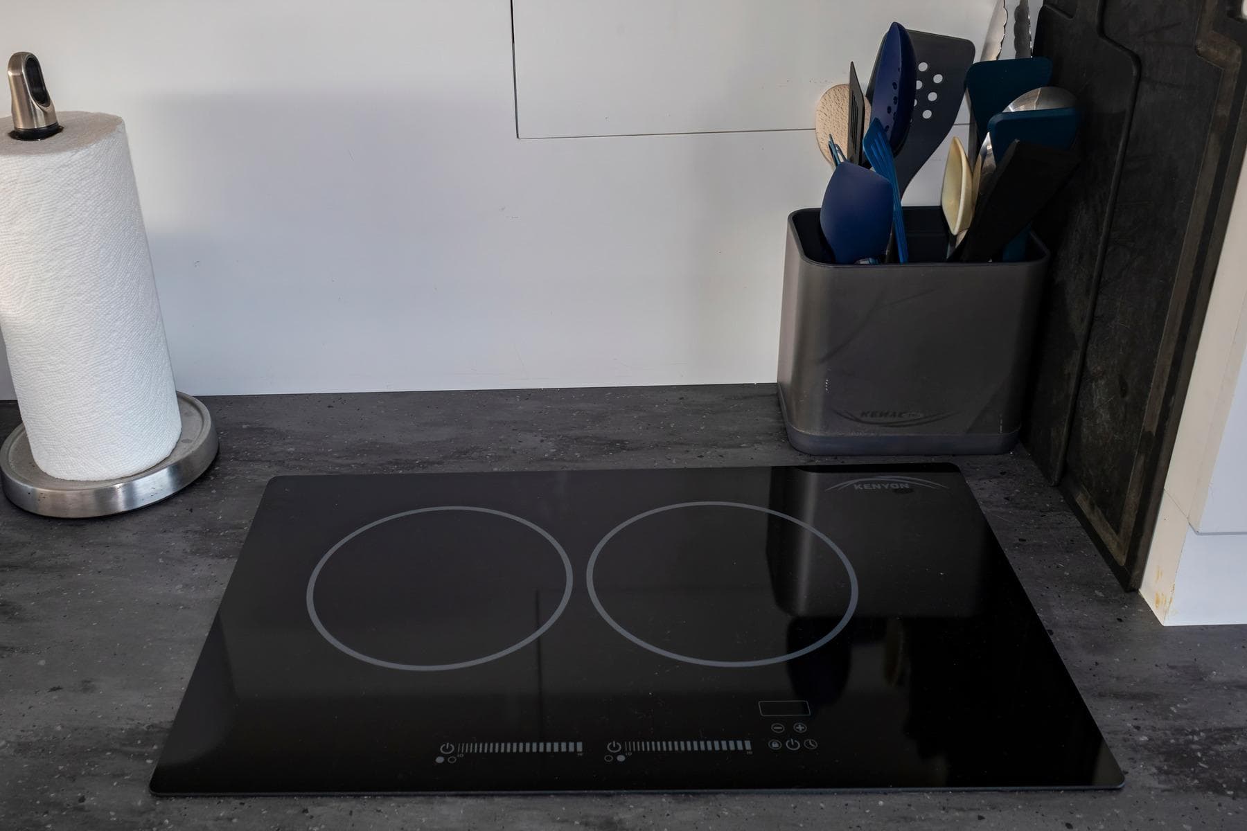 Modern kitchen countertop with induction cooktop, utensils, and paper towel holder on Fountaine Pajot MY5.