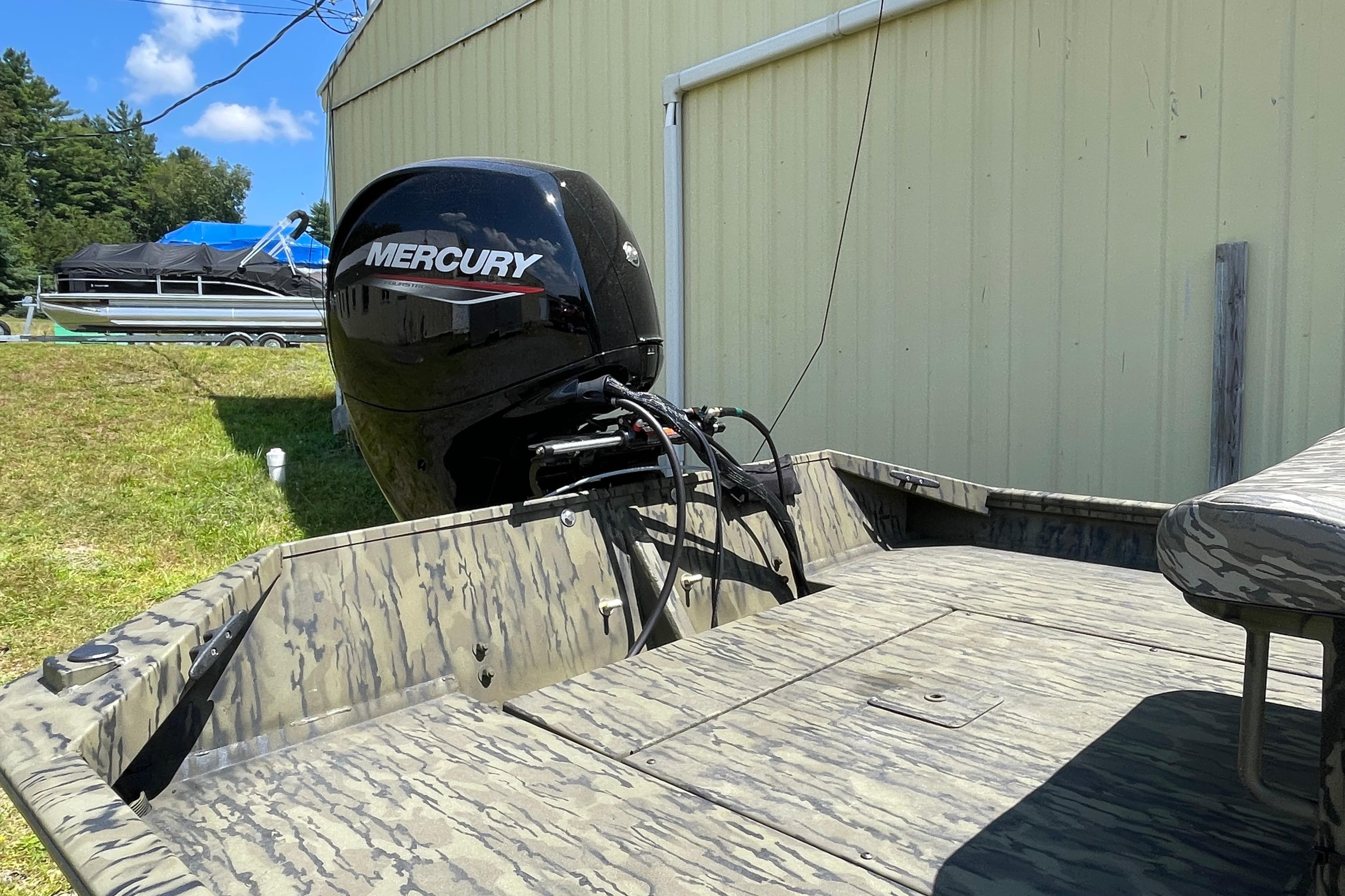 2026 Lund 1870 Predator CC boat with Mercury engine, camo design, parked outdoors.