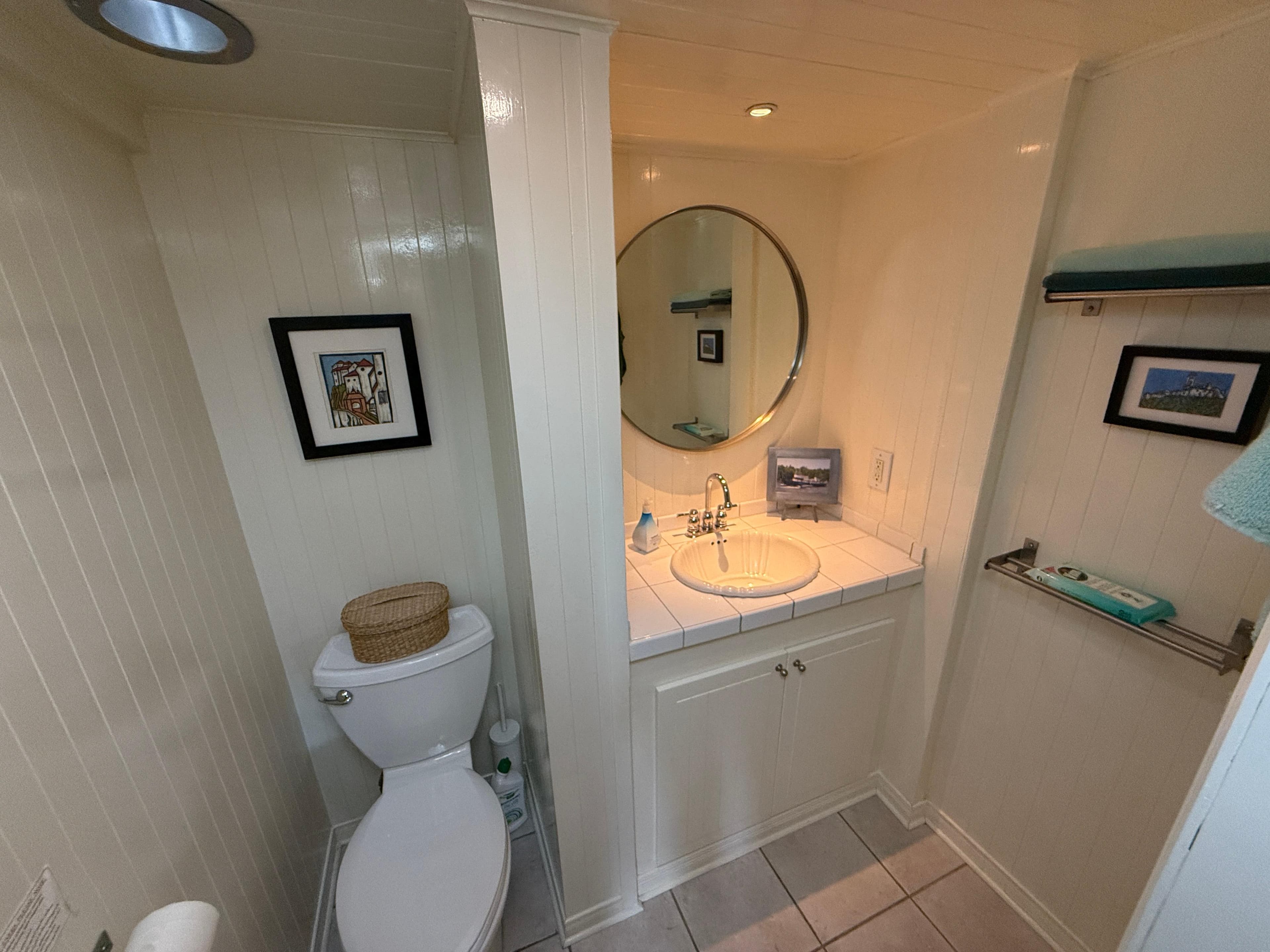 Small, vintage-style bathroom with round mirror, white fixtures, and framed artwork.