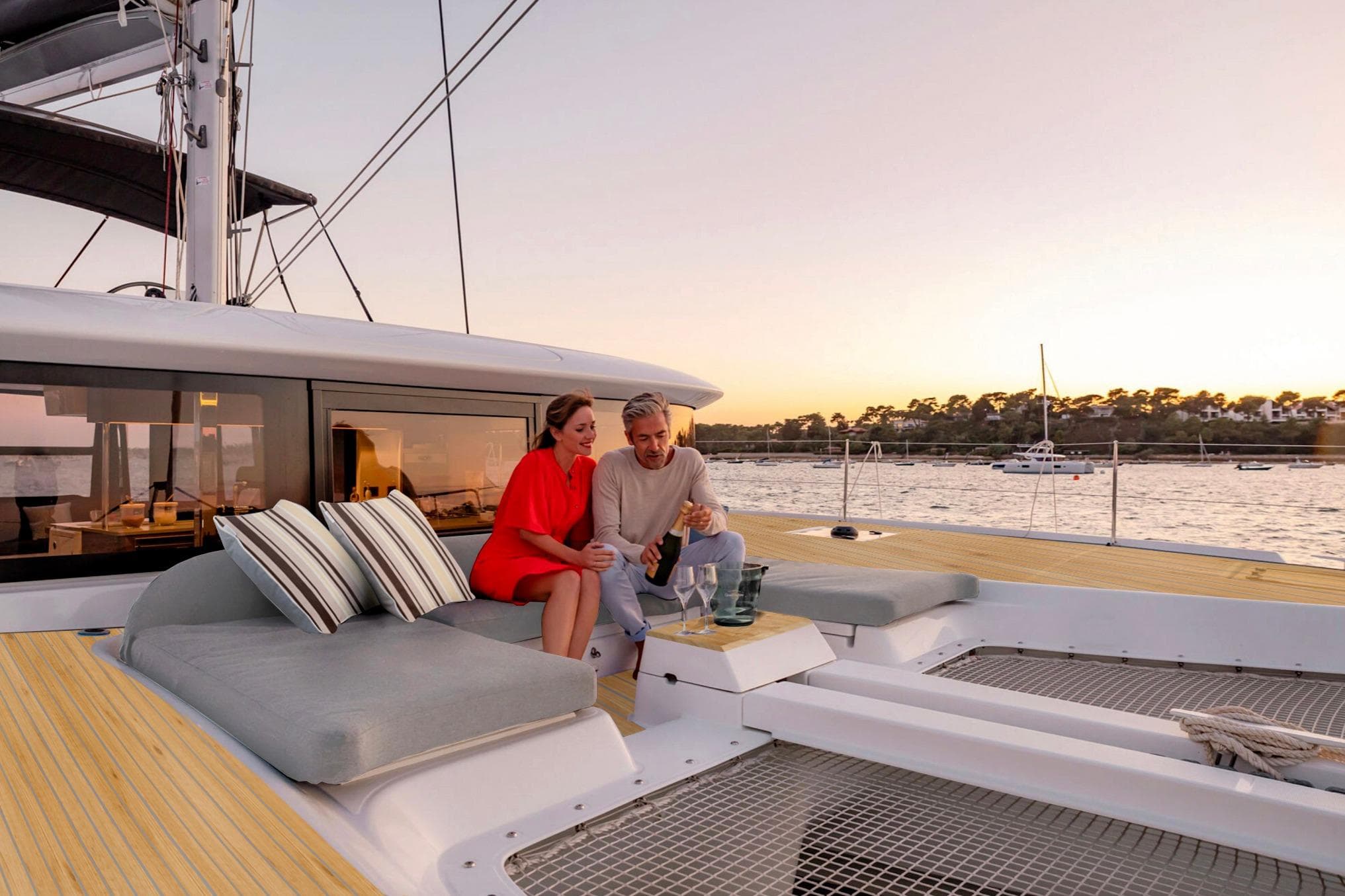 Couple relaxing on 2024 Lagoon 42 catamaran at sunset, enjoying a scenic view.
