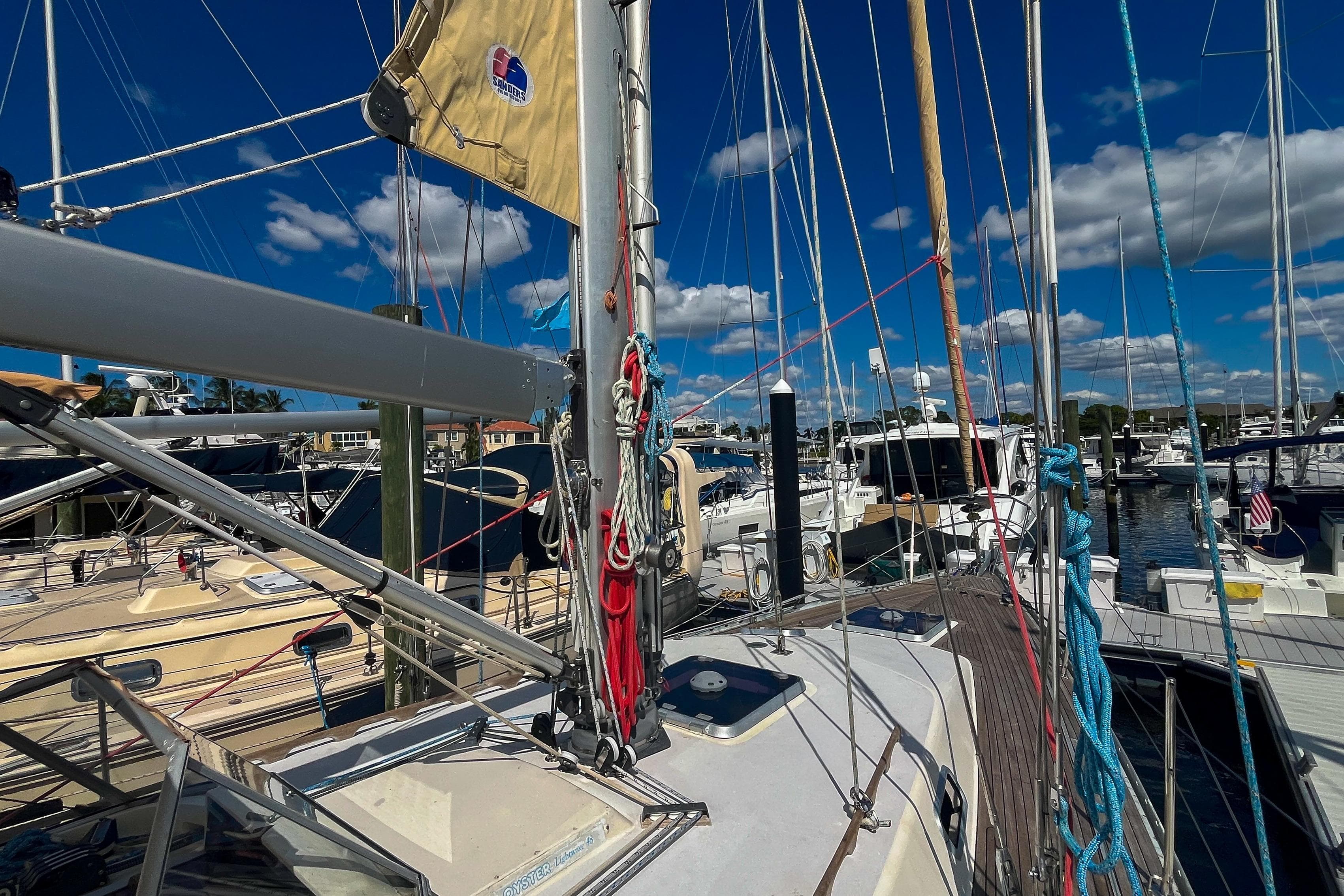 Sailboat deck view of 1991 Oyster LW48 in marina, under clear blue sky.