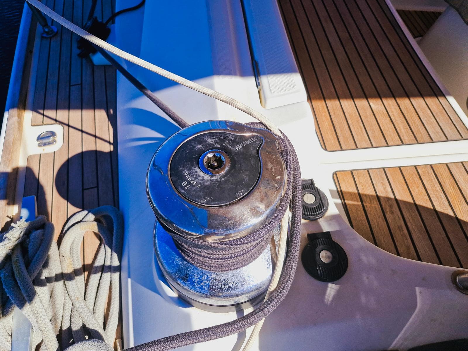 Winch on Jeanneau 53 sailboat deck, 2015 model, with ropes and wooden flooring.