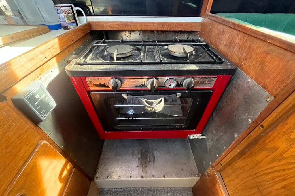 1978 CAL 34 boat kitchen with a red stove and oven, wooden cabinetry, and control panel.