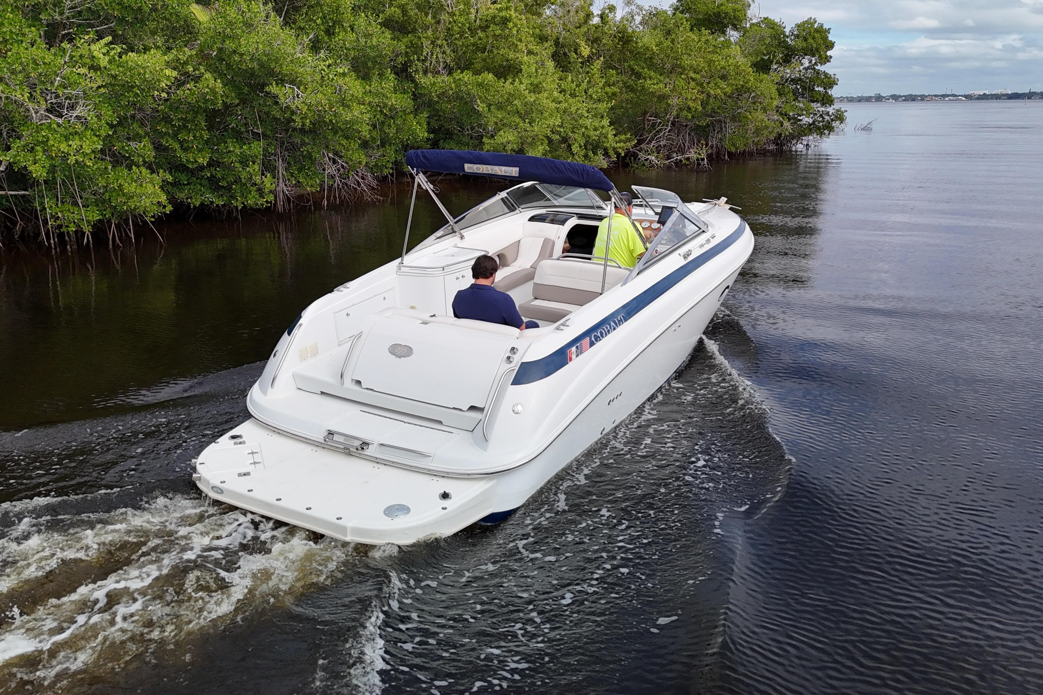 1999 Cobalt 293 boat cruising on a calm river near lush greenery.