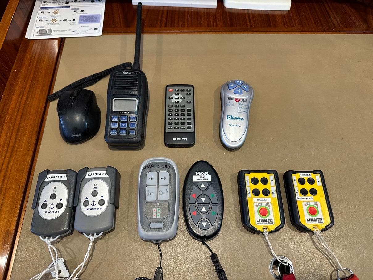 Various remote controls and devices on a table, including a radio and mouse, Amel 64, 2015.
