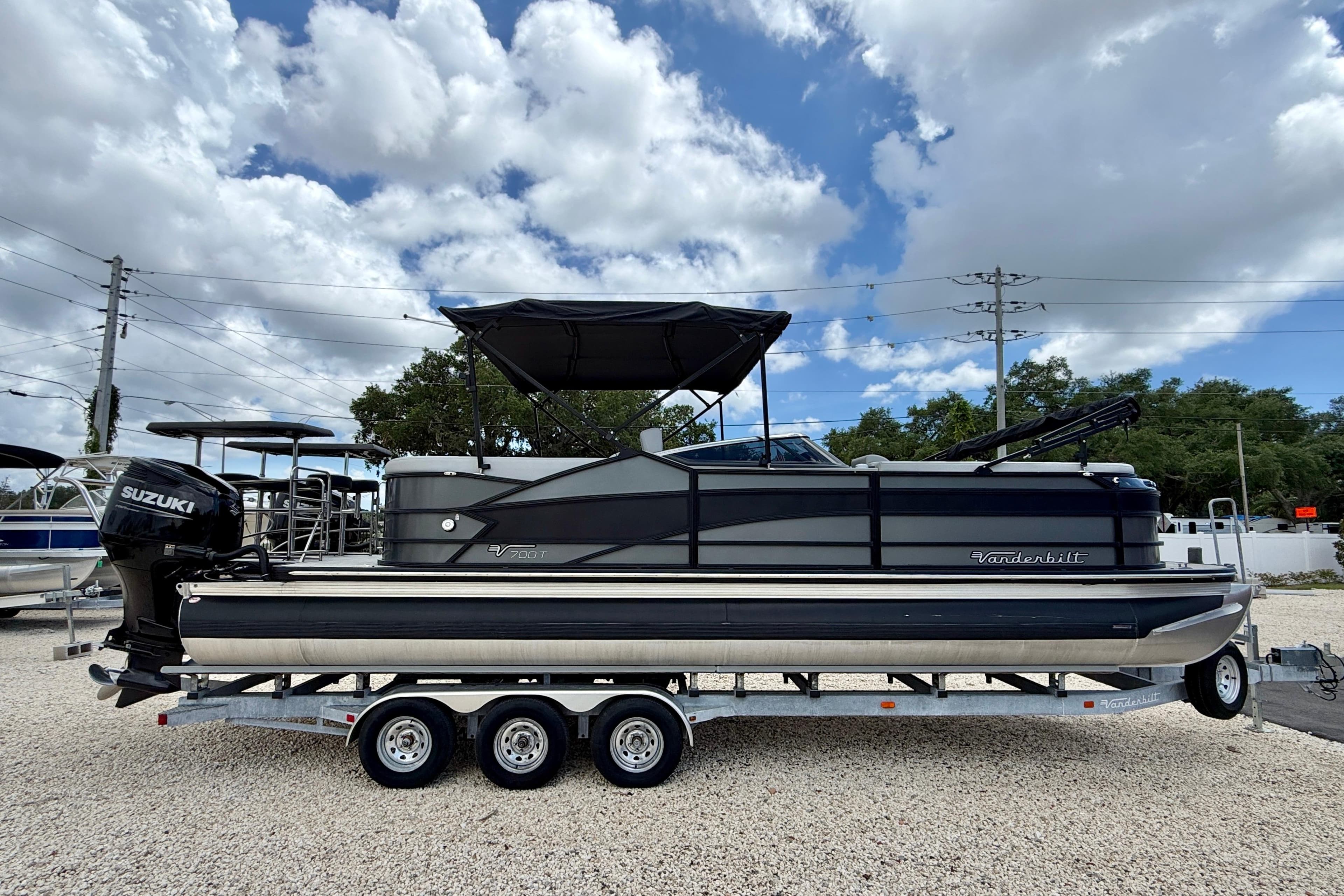 2025 Vanderbilt 700T pontoon boat on trailer, featuring Suzuki outboard motor, under cloudy sky.