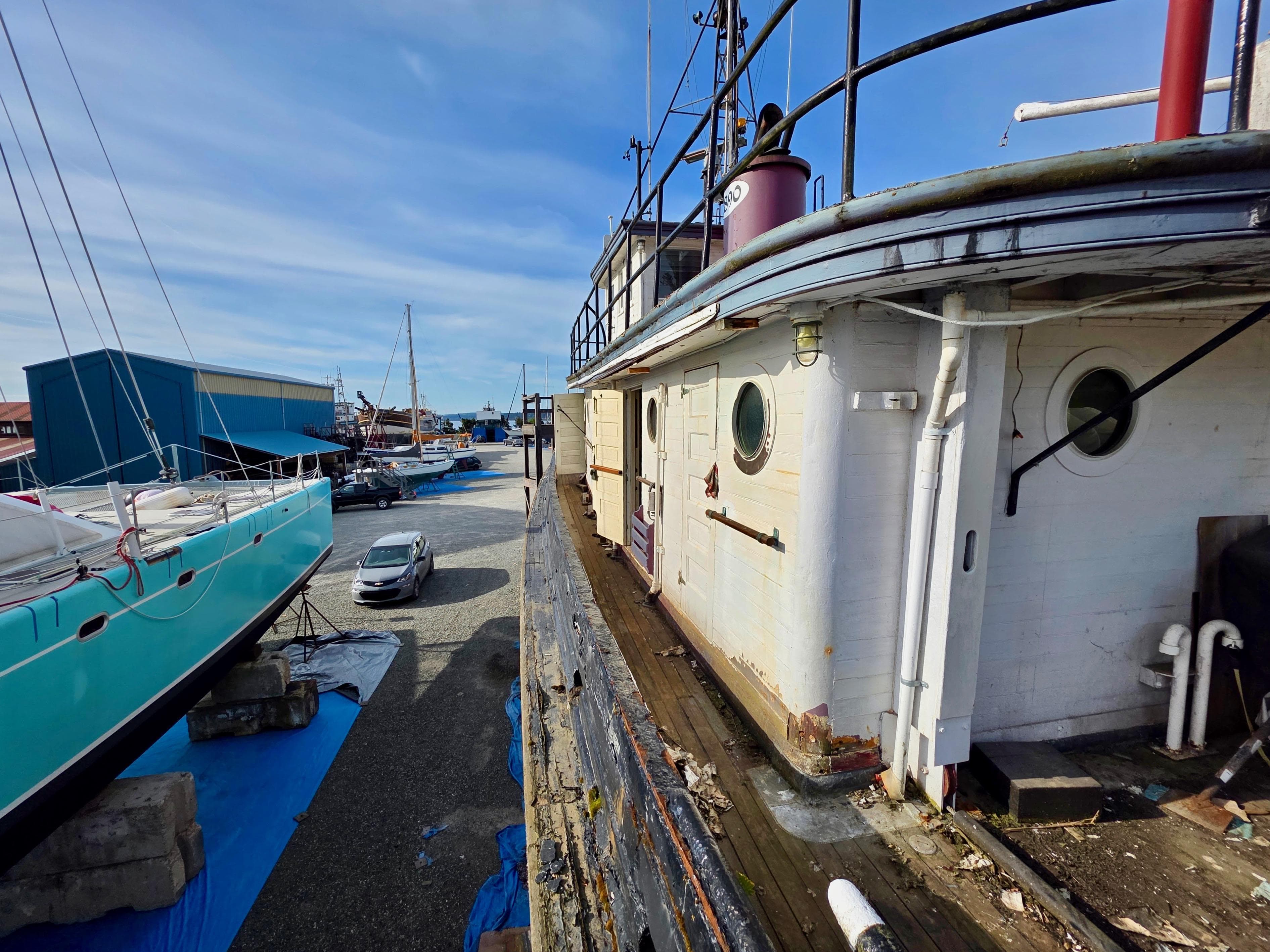 Restored 1890 custom tugboat docked beside modern yachts in a shipyard.