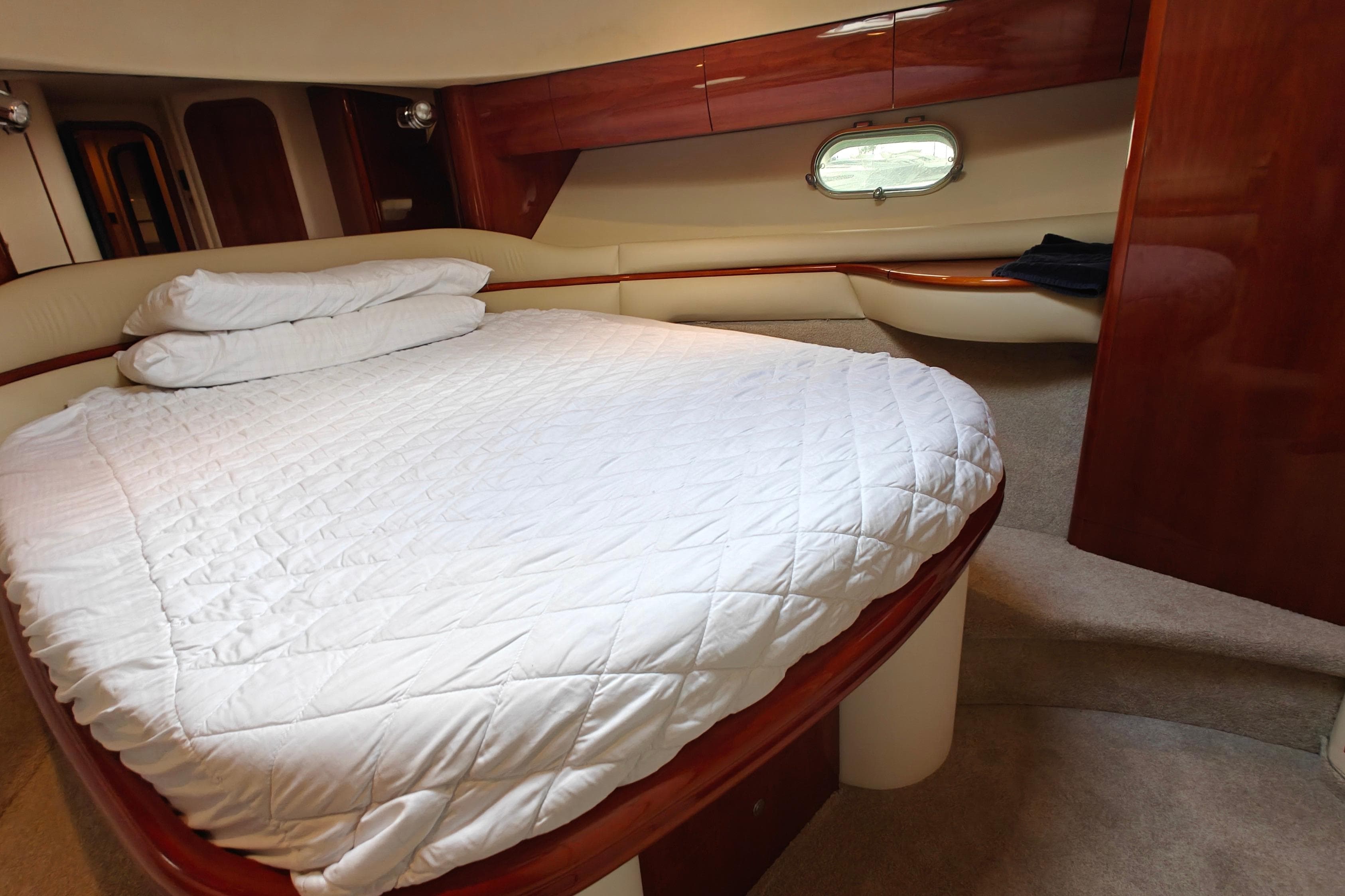 Luxurious cabin interior of 2003 Princess 65 yacht with cozy bed and elegant wood finish.