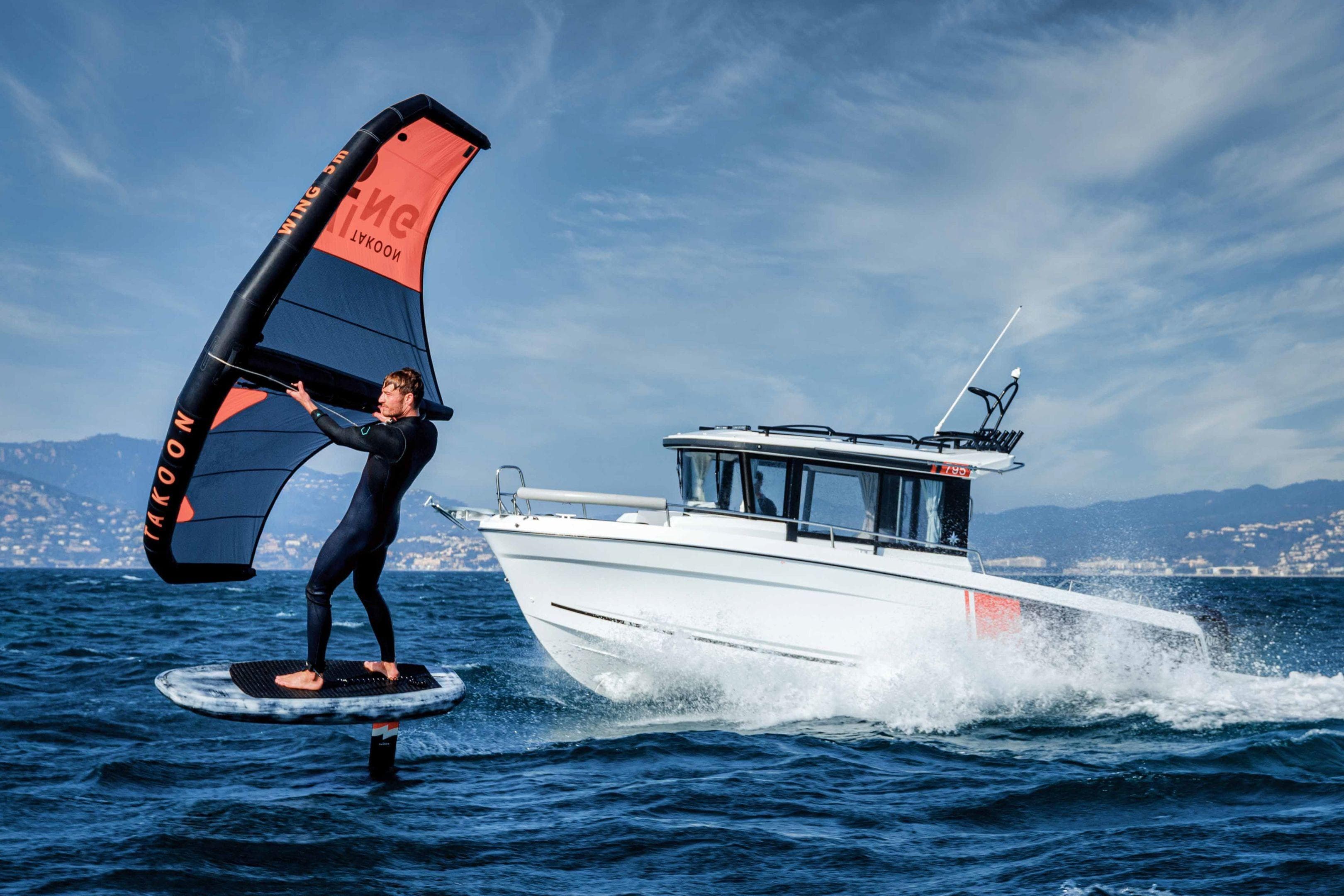 2026 Jeanneau NC 795 Sport cruising alongside a wing surfer on open water.