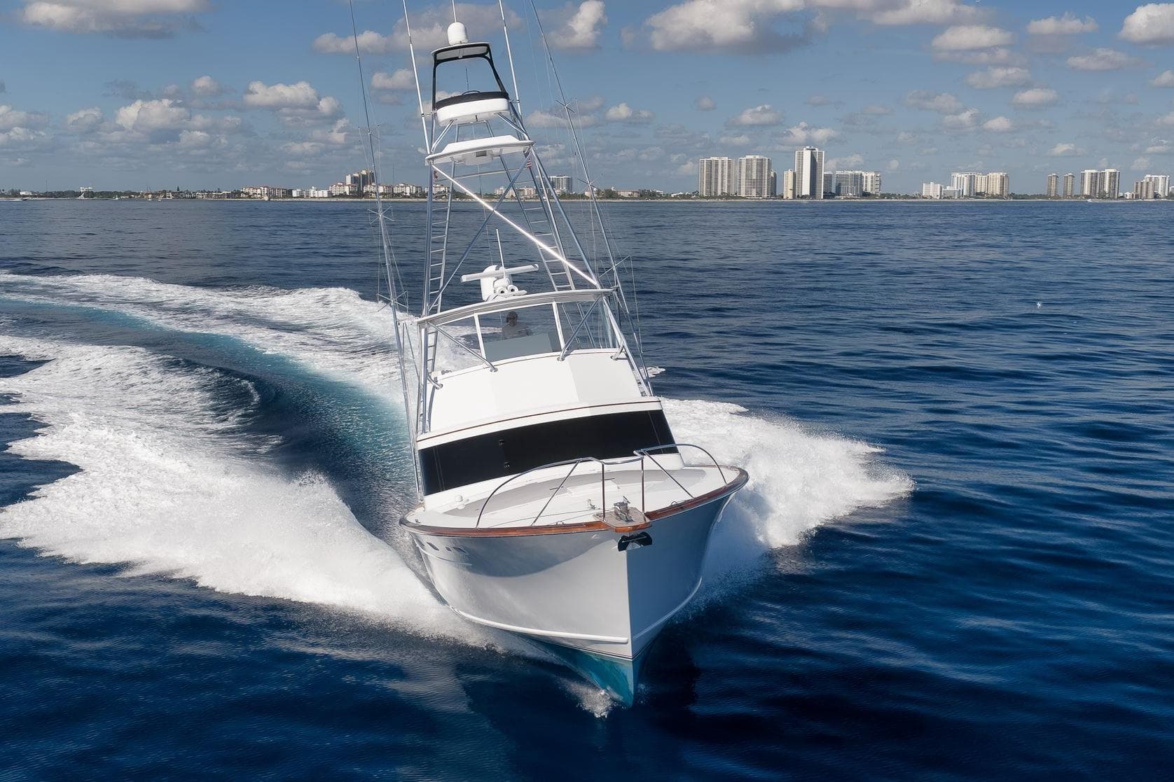 1998 Rybovich Convertible yacht cruising on open water with city skyline in background.