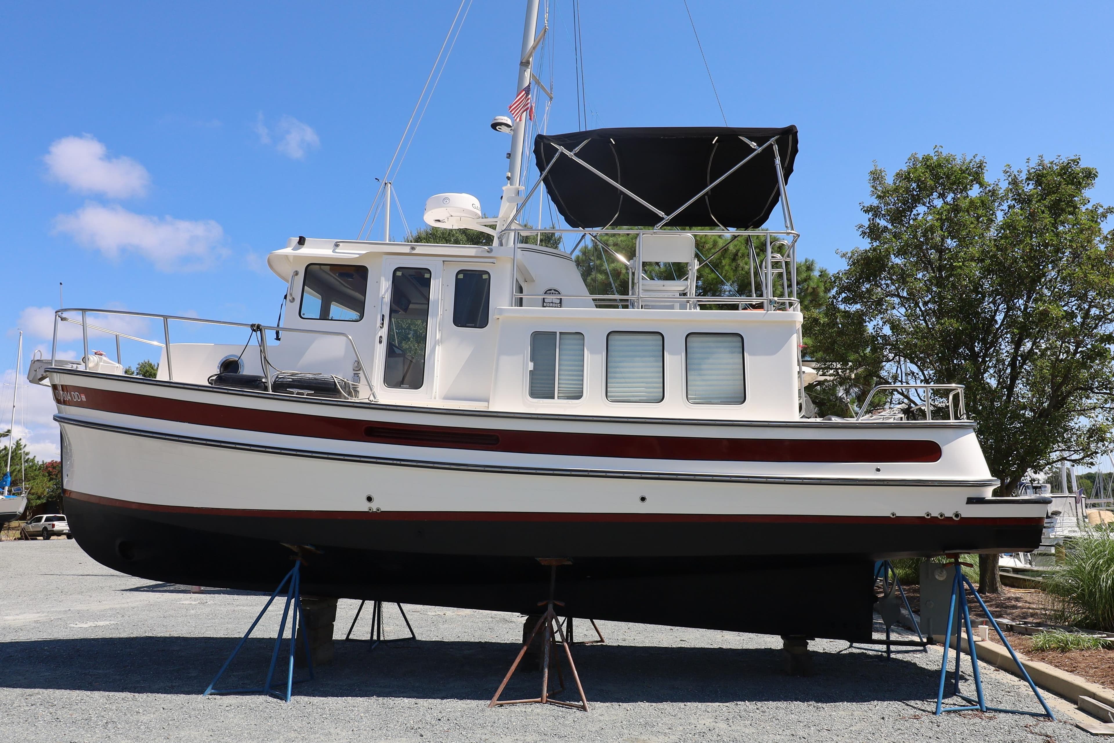 2007 Nordic Tug 32 boat on dry dock, white with red accents, under clear blue sky.