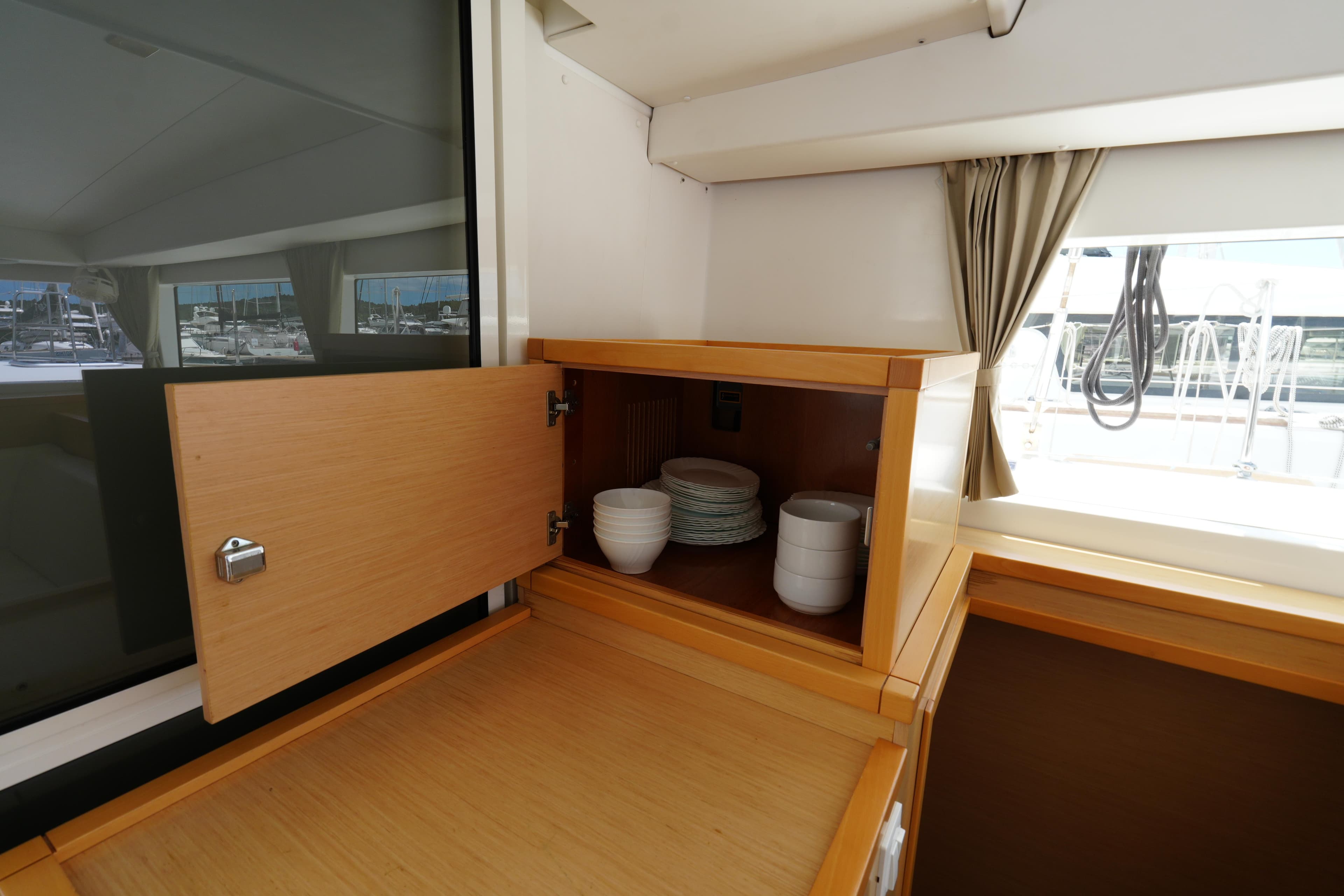 Interior of 2015 Lagoon 400 S2 yacht showing open cabinet with dishes and cups.