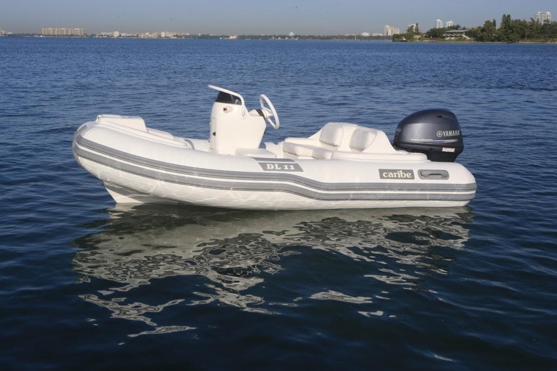 2025 Caribe DL11 inflatable boat on calm water with Yamaha outboard motor.