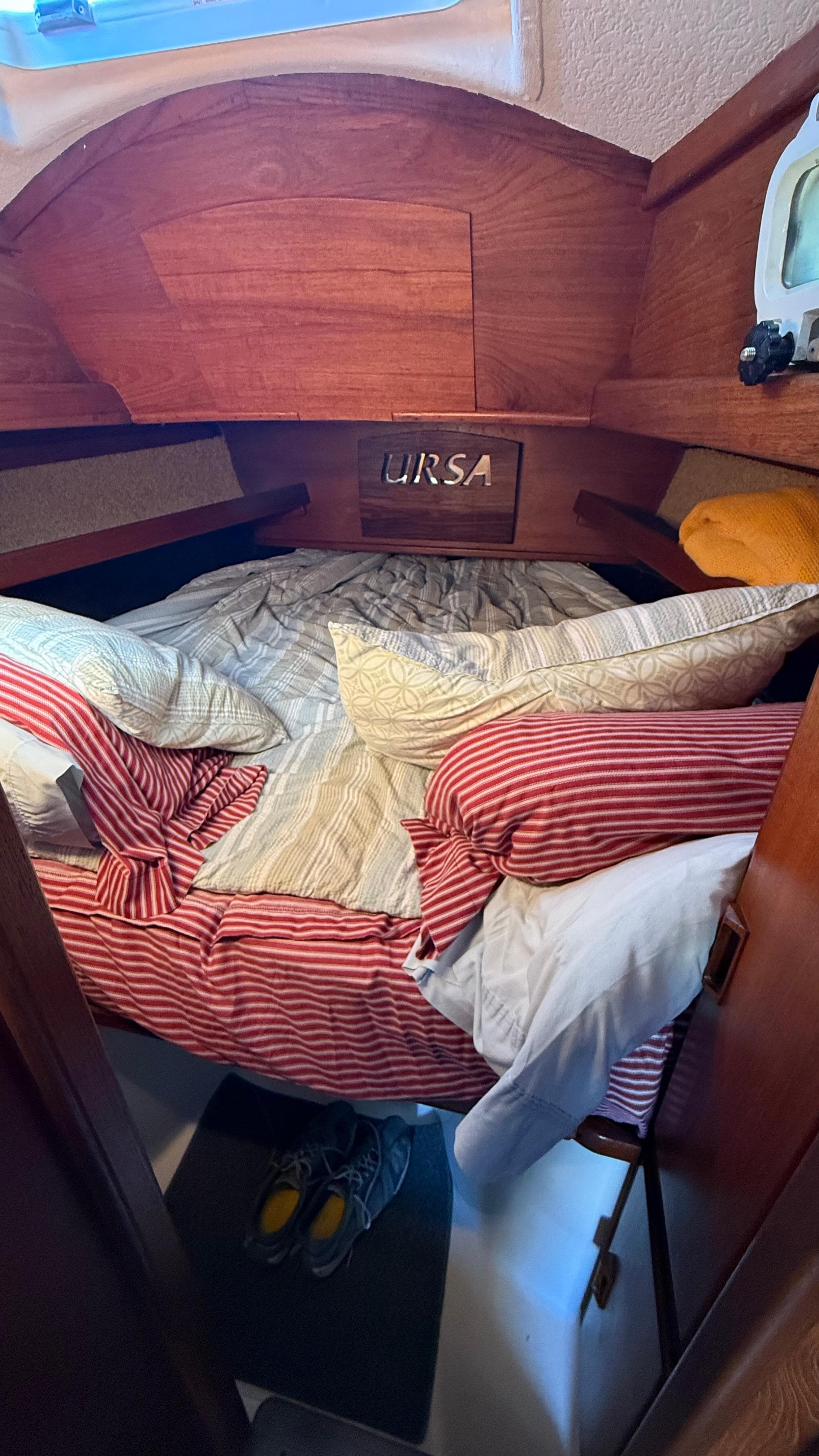 Cozy cabin interior of 1984 Cascade 36 sailboat with striped bedding and wooden accents.