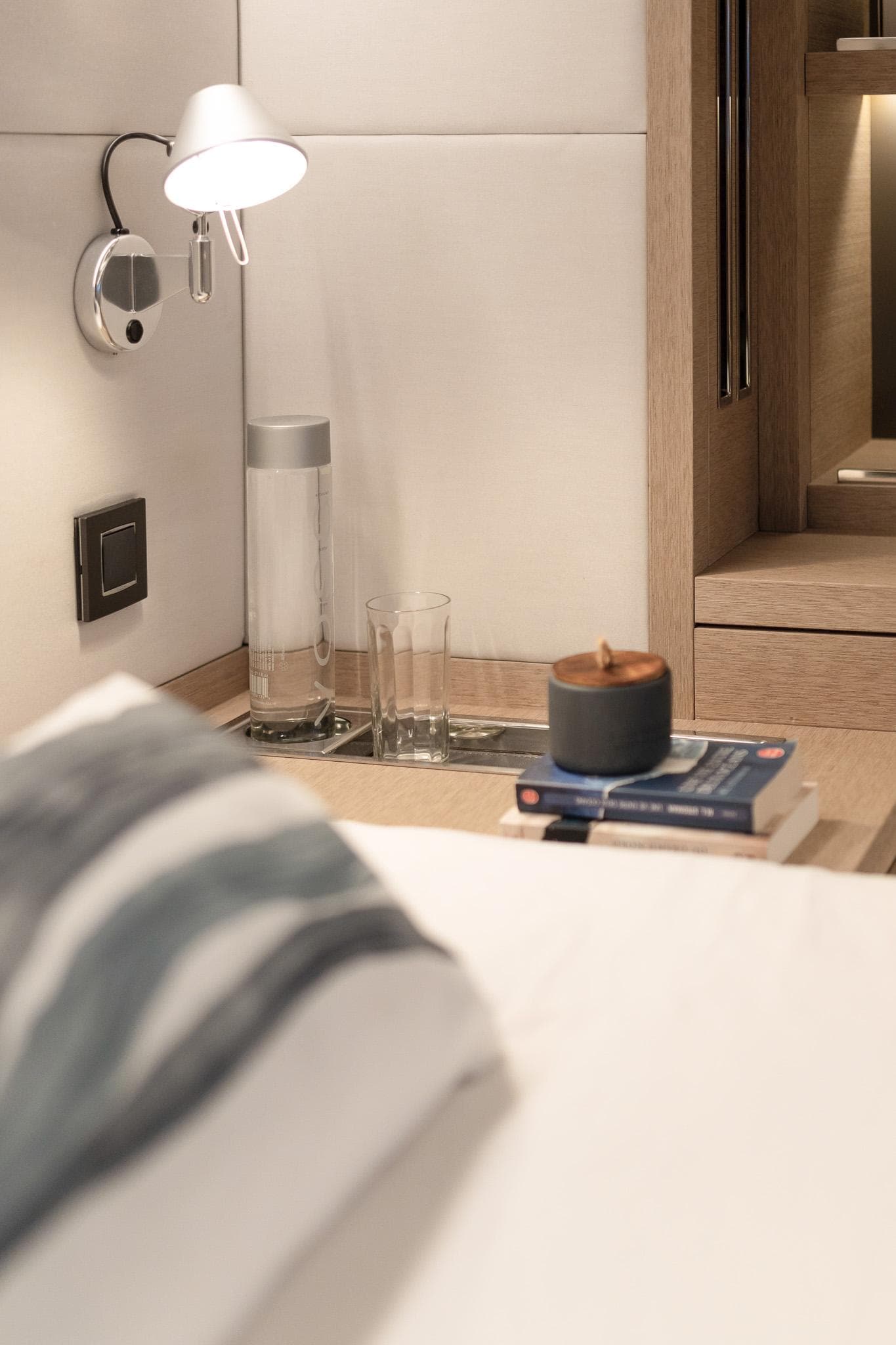 Luxurious Lagoon SIXTY 5 yacht interior, featuring a cozy bedside setup with books and a lamp.
