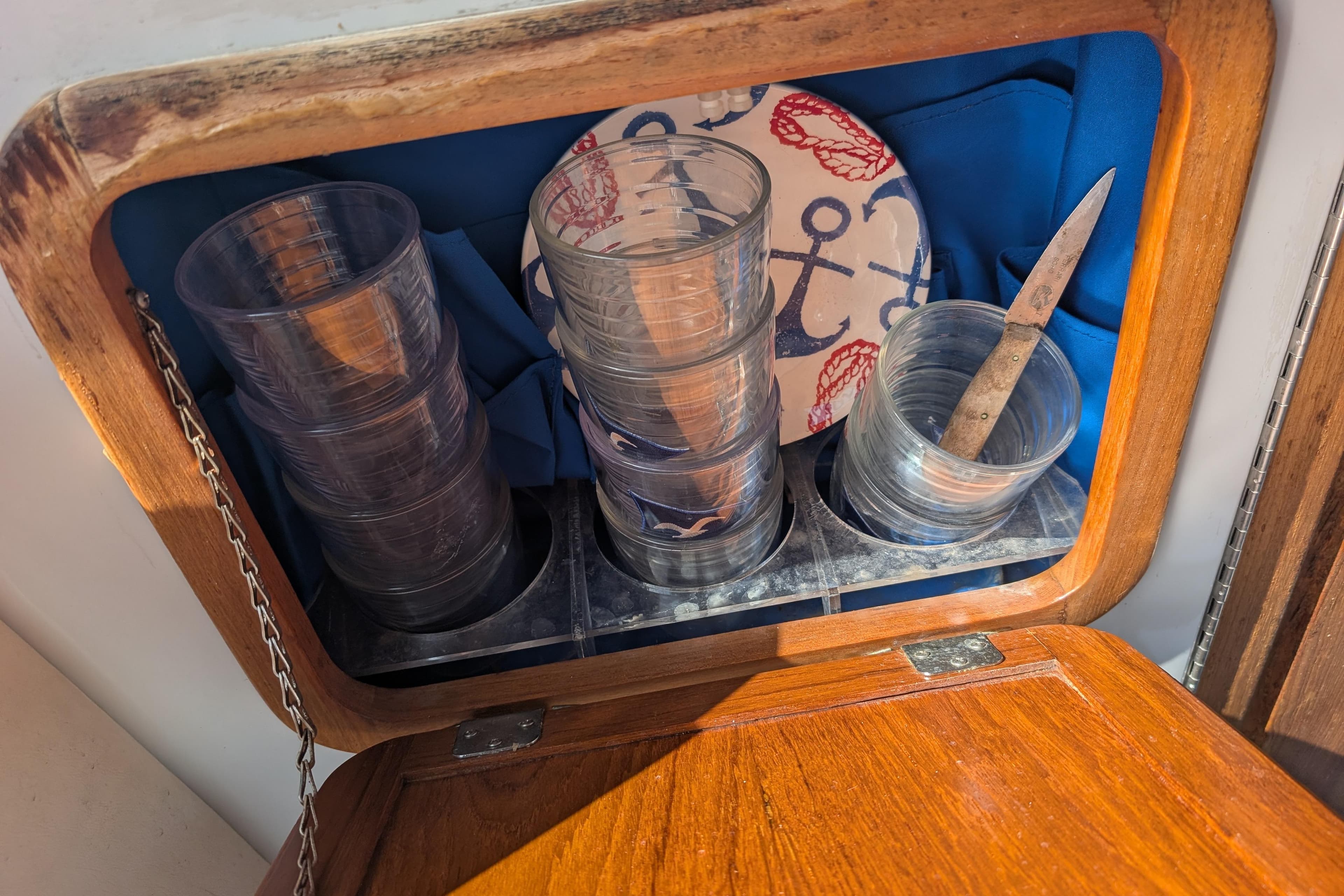 Wooden cabinet on 2007 Duffy Cuddy Cabin 22, storing cups, knife, and nautical-themed plate.