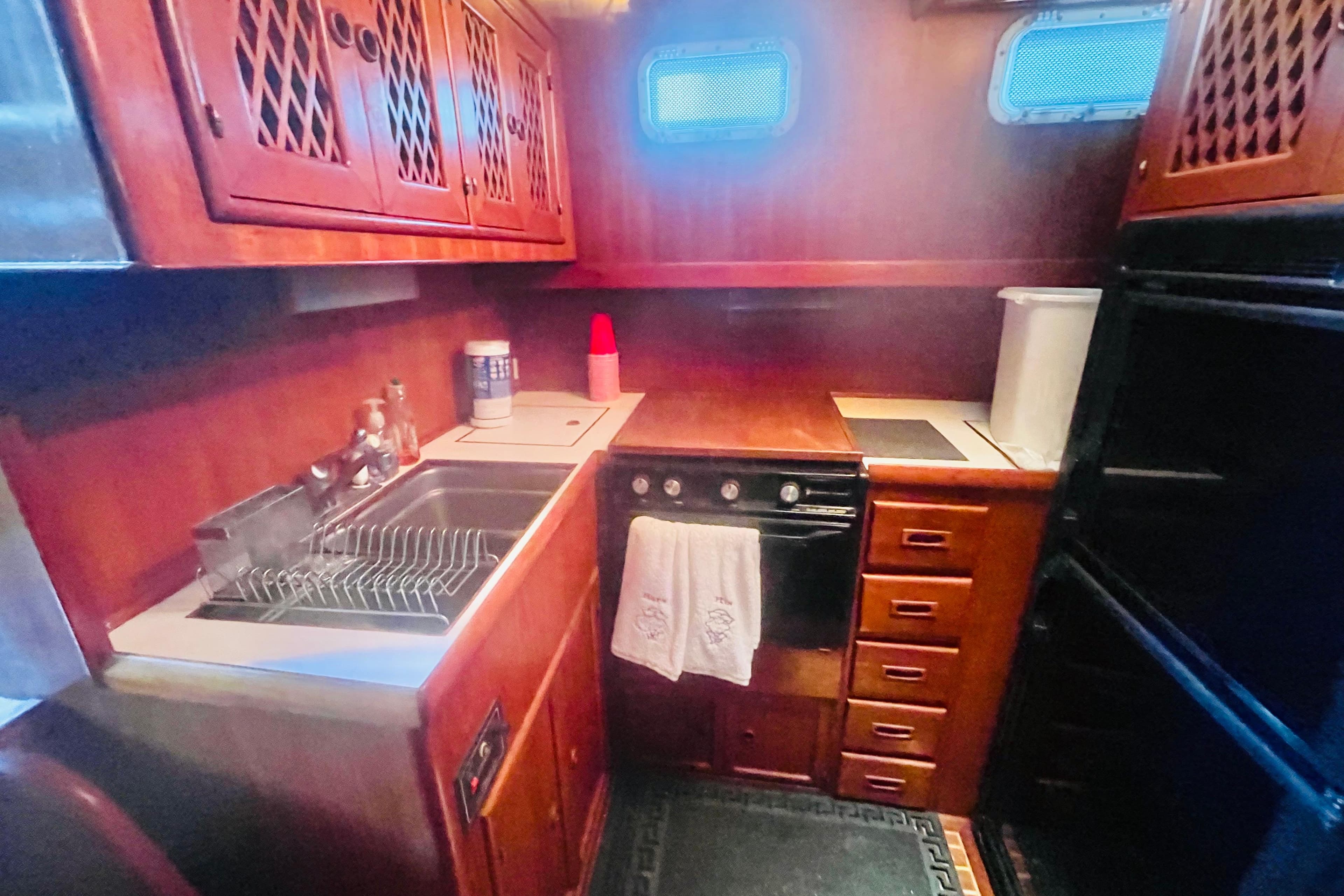 1986 Tung Hwa aft cabin kitchen with wooden cabinetry, sink, stove, and storage drawers.