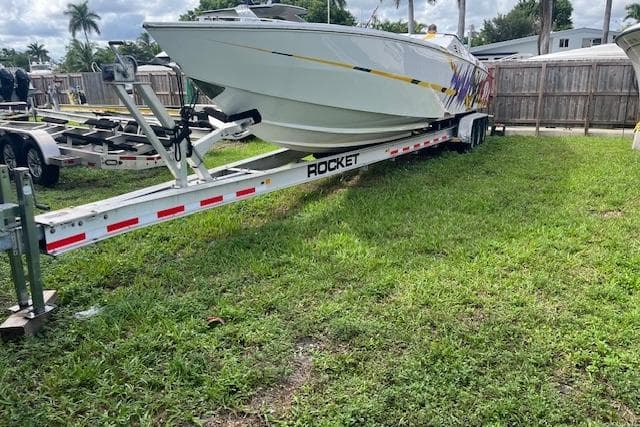 2000 Cigarette Top Gun T/S 38 boat on Rocket trailer, parked on grass.