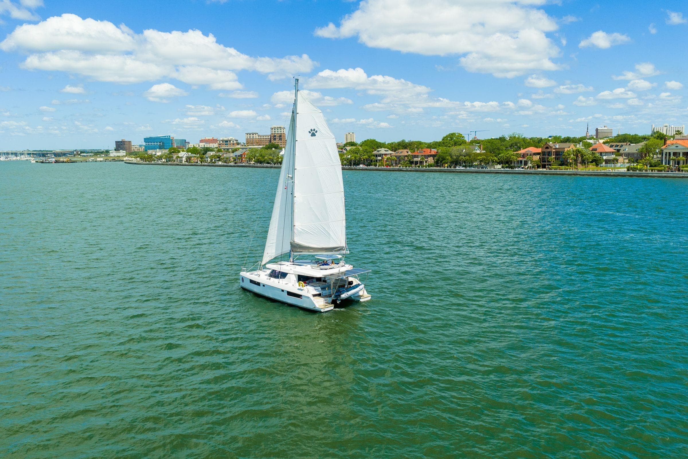 Sailing catamaran Leopard 45 on calm waters near a coastal cityscape, under a blue sky.