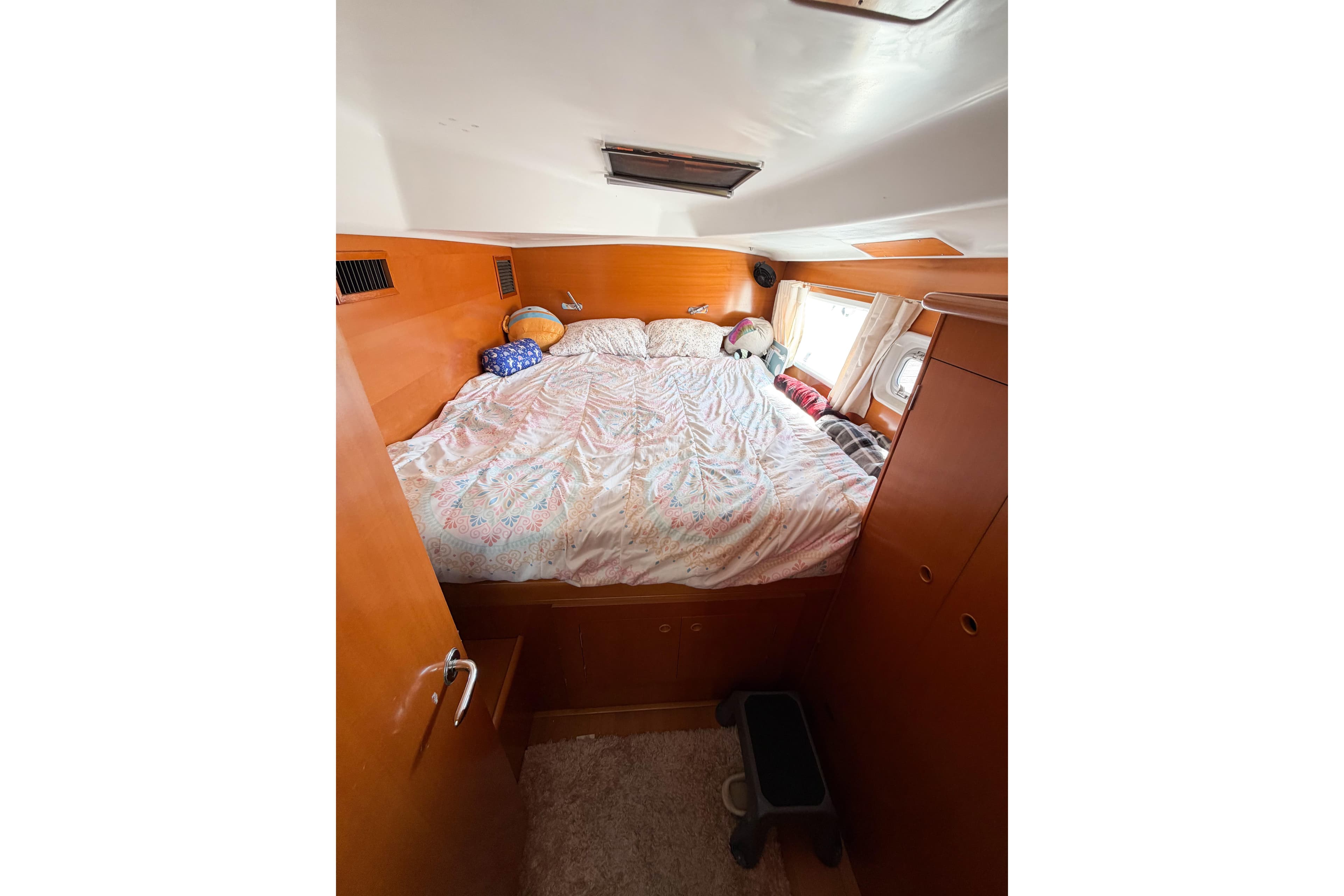 Cozy bedroom interior of 2005 Lagoon 380 S2 catamaran with wooden finish and porthole window.