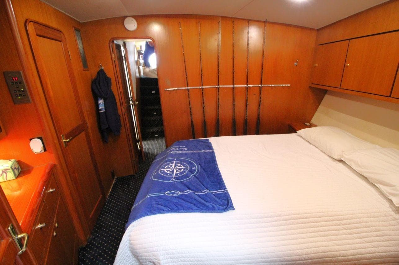 Cozy bedroom in 1999 Ocean Yachts 60 Super Sport with wooden cabinetry and fishing rods.
