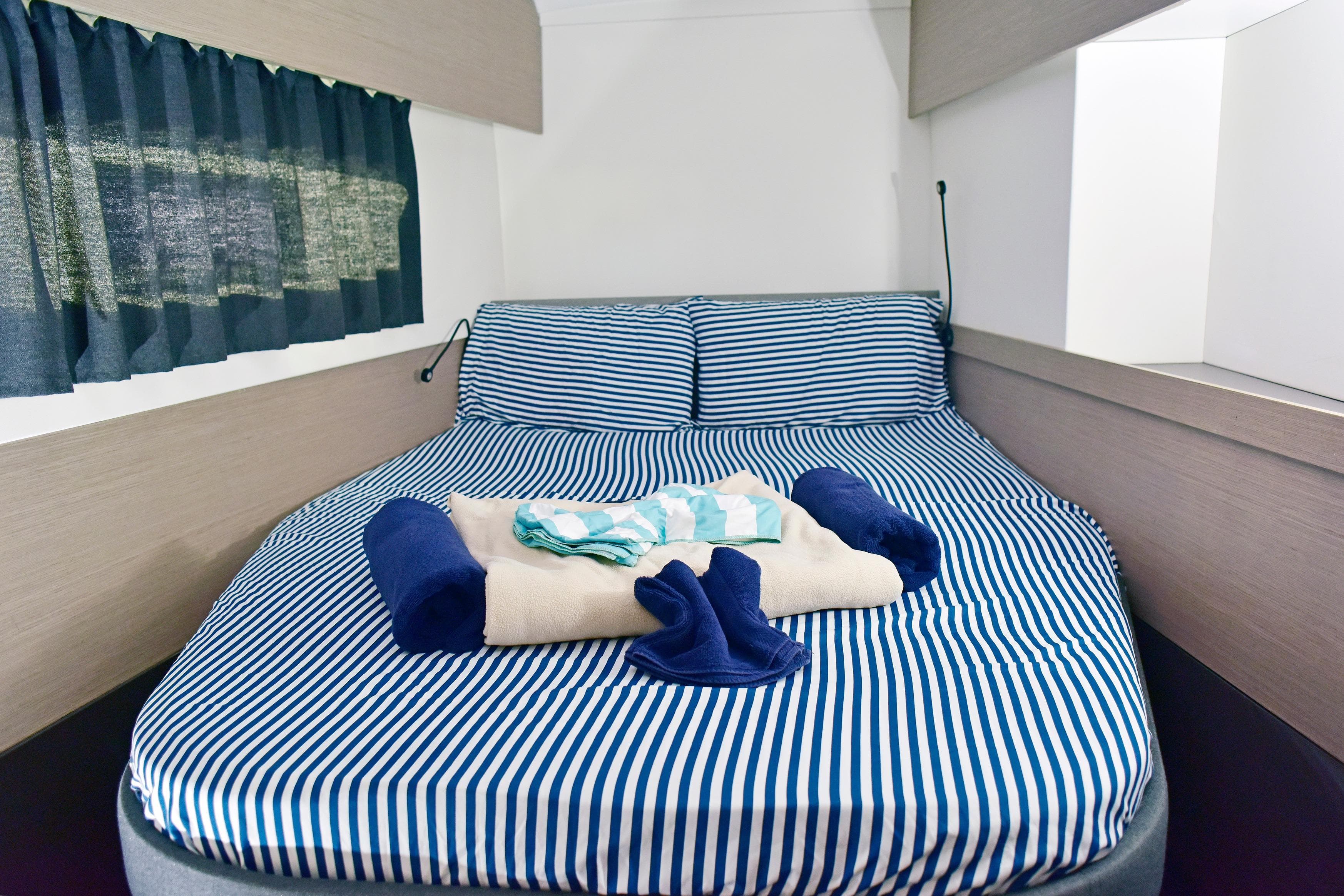 Cozy cabin interior of 2022 Fountaine Pajot Astrea 42 with striped bedding and folded towels.