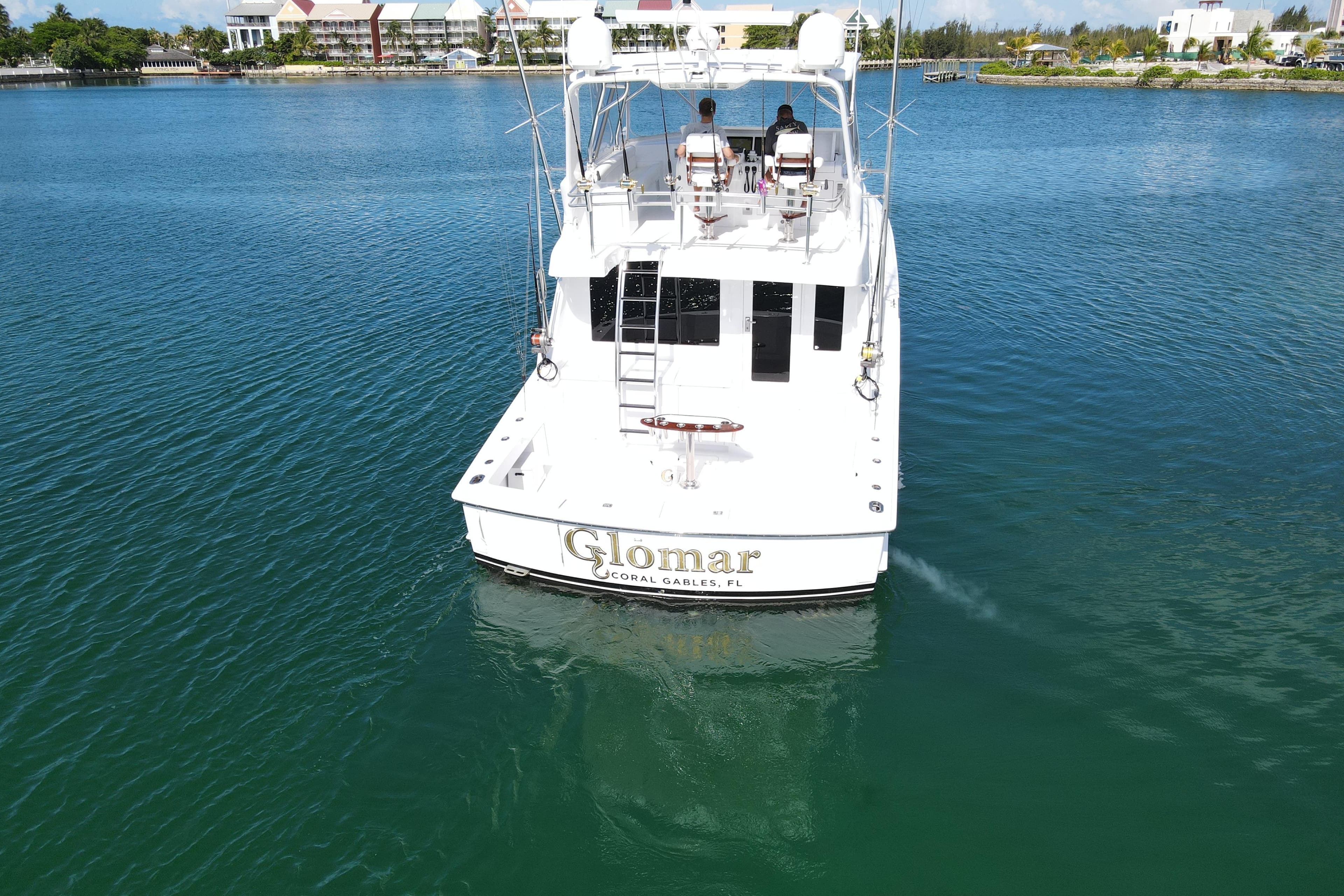2004 Hatteras 60 Convertible yacht on calm water, rear view, with two people seated.