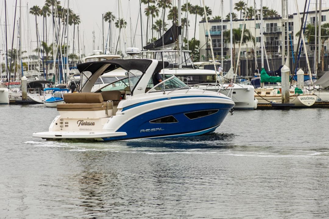 2014 Regal 32 Express boat cruising in a marina with sailboats in the background.