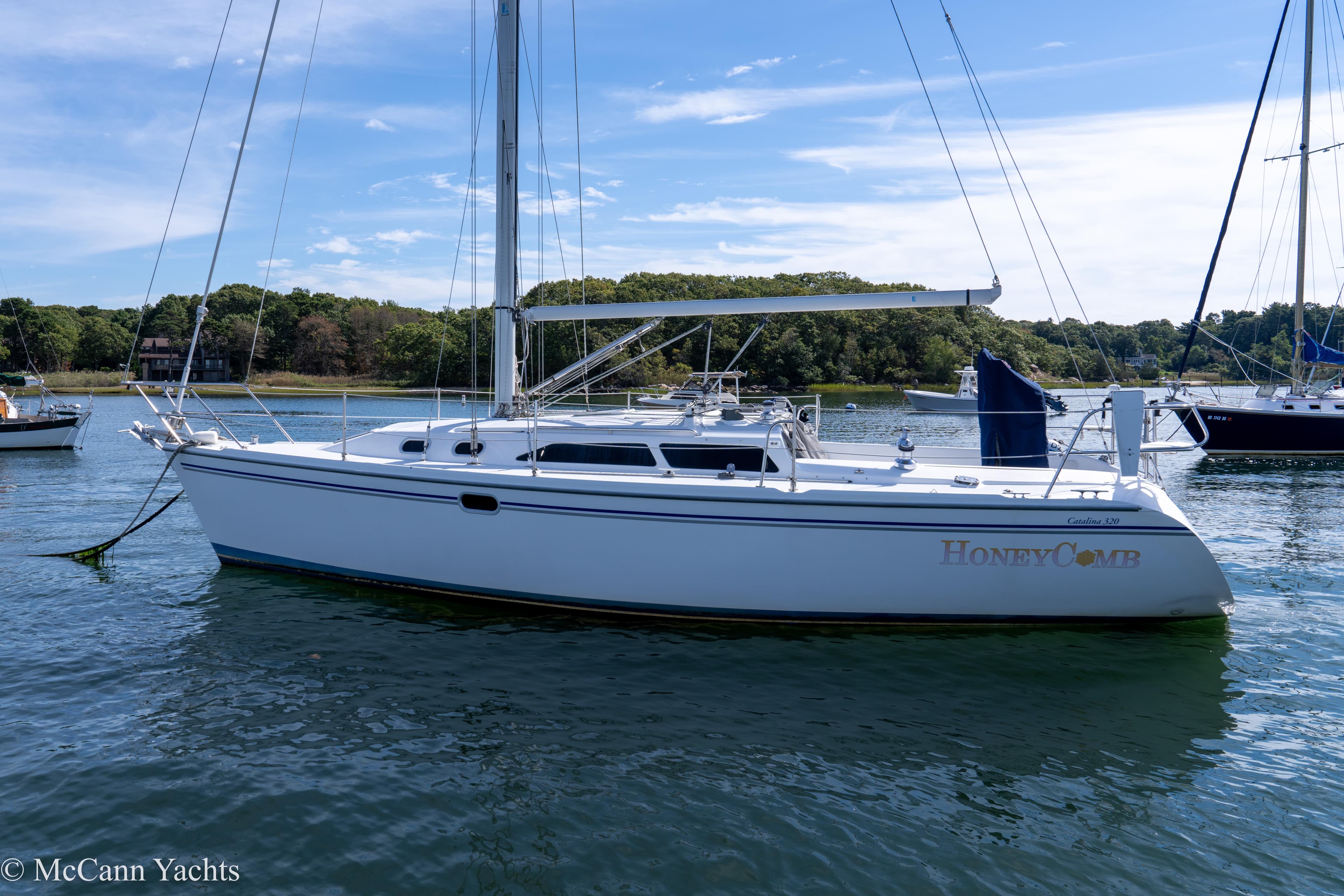 2003 Catalina 320 sailboat named HoneyComb on calm water, clear sky background.