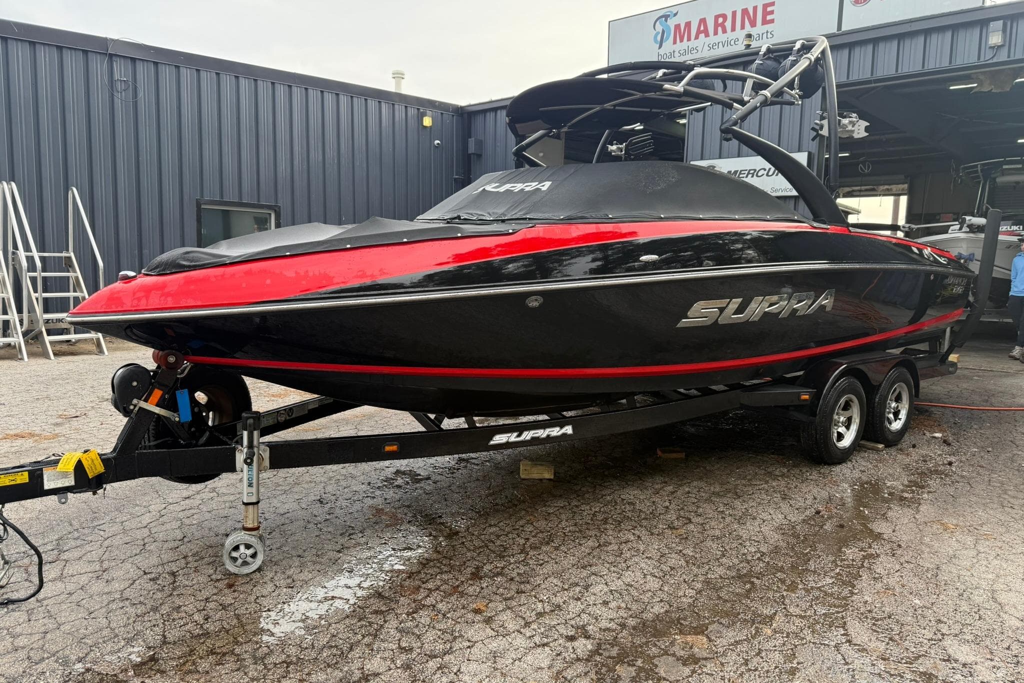 2011 Supra Launch 242 boat in black and red, parked on a trailer outside a marine service shop.