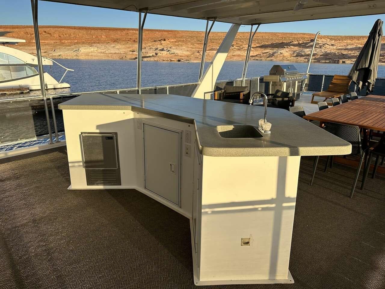 Outdoor kitchen on 2005 Sumerset Top Hat houseboat, featuring sink and counter, docked by a lake.