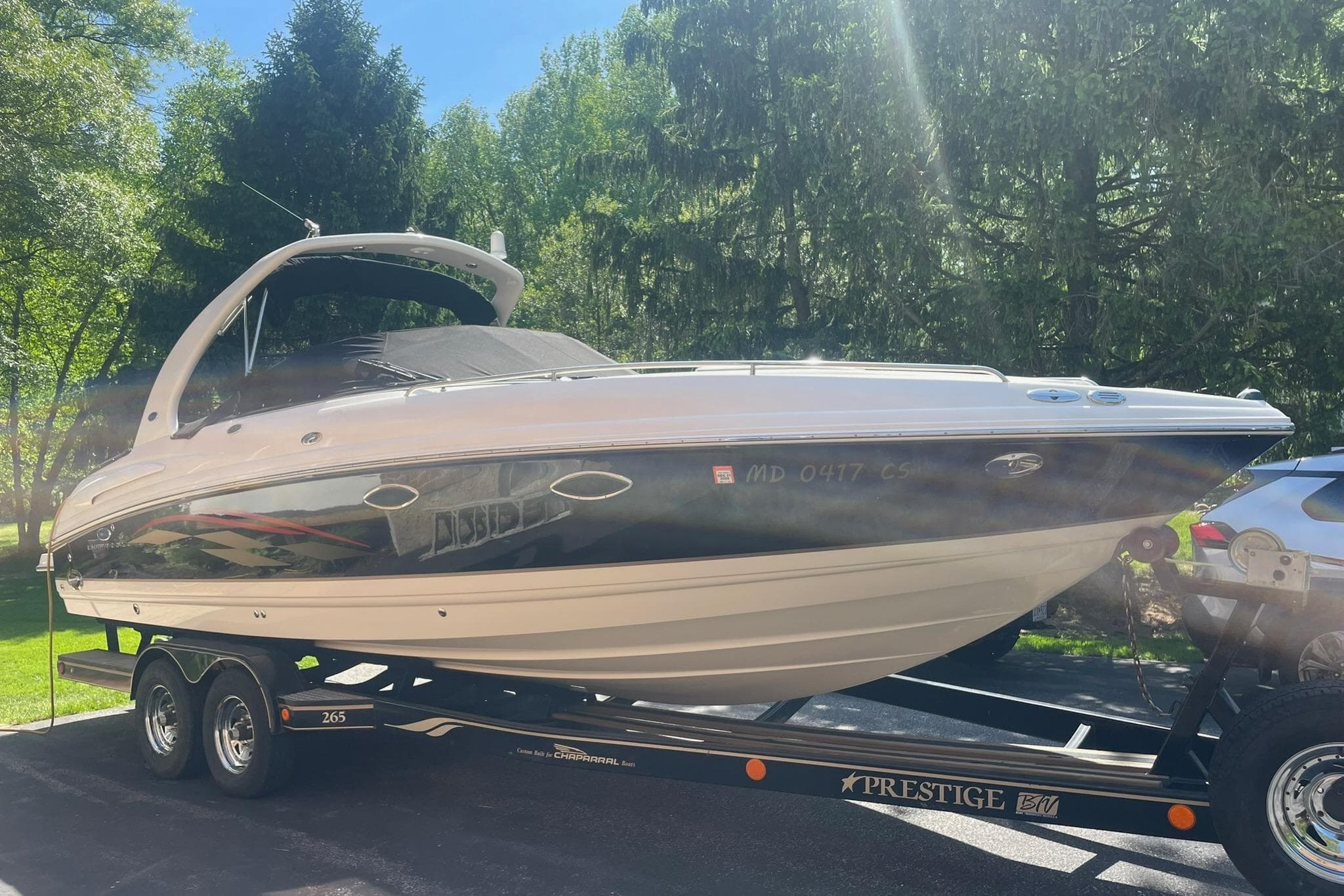 2005 Chaparral 265 SSi boat on trailer, parked outdoors in a sunny, wooded area.