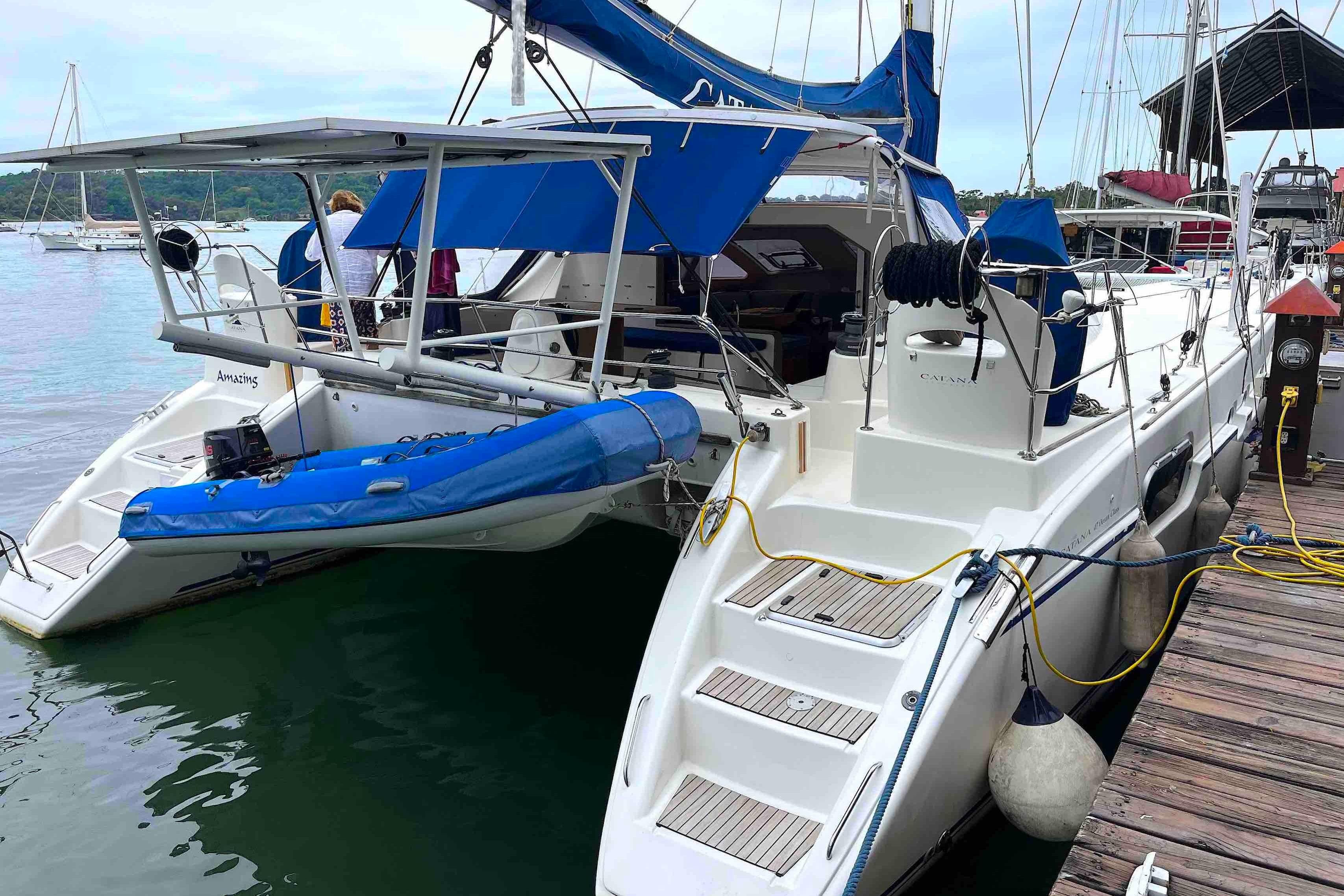 Catana 471 catamaran from 2004 docked with blue covers and inflatable boat.