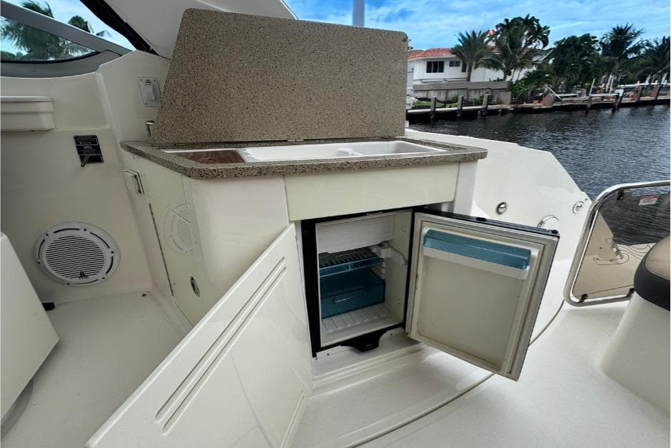 2016 Sea Ray 350 Sundancer boat kitchenette with open mini-fridge and sink by the water.