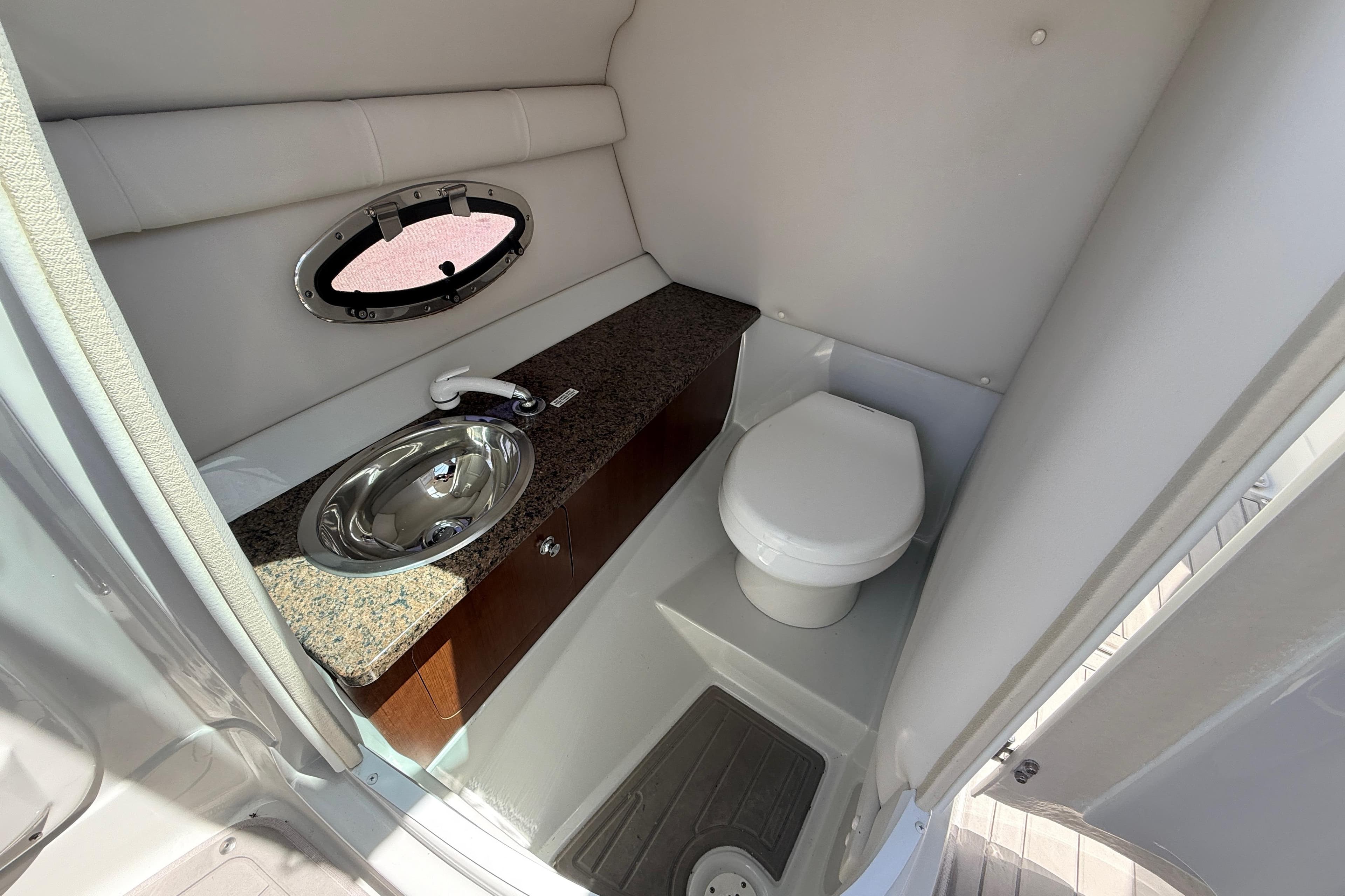 2018 Crownline Eclipse E26 XS boat bathroom with sink, toilet, and porthole window.